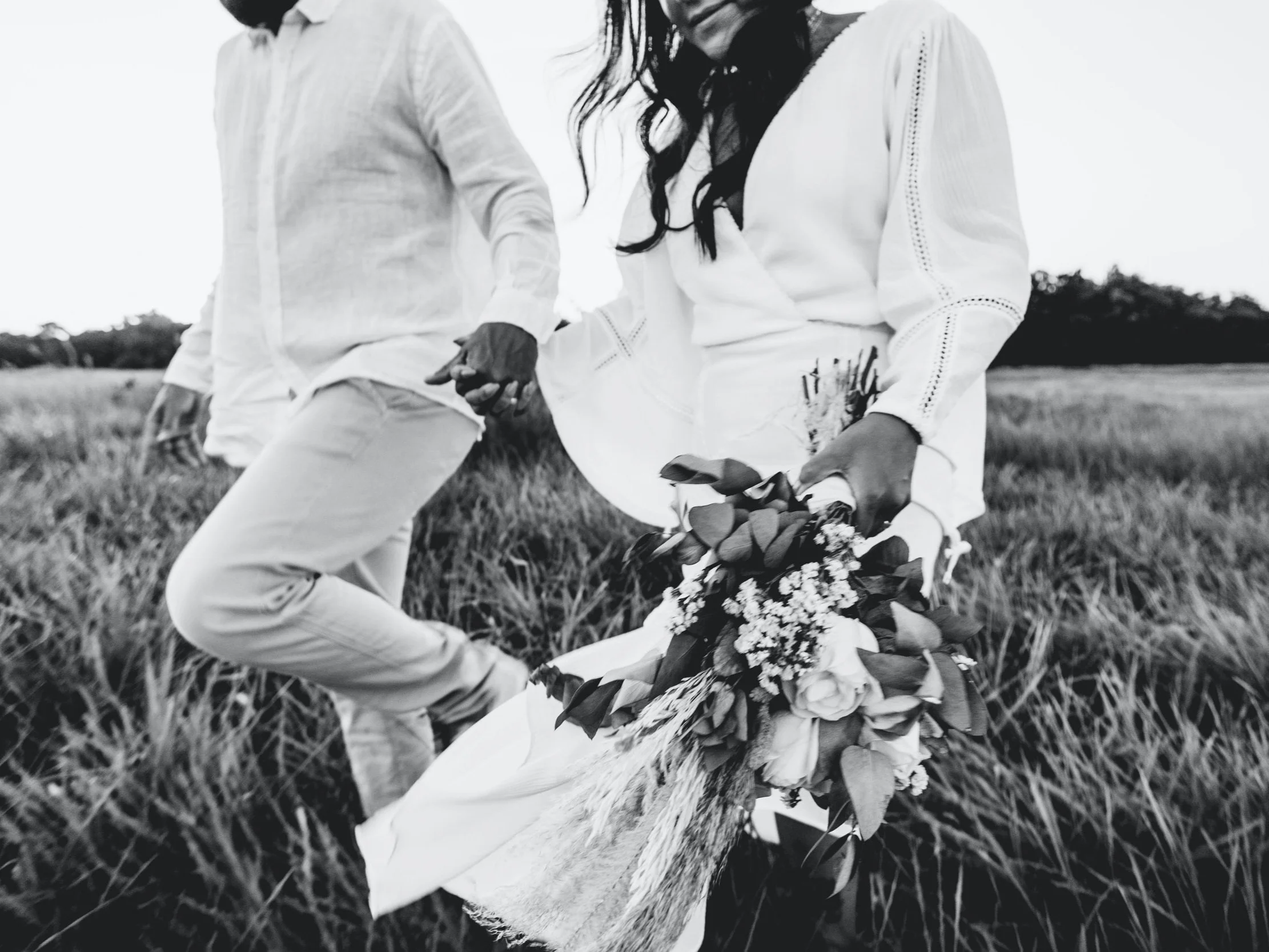 A couple holding hands in a field with a bouquet of flowers, black and white photo.