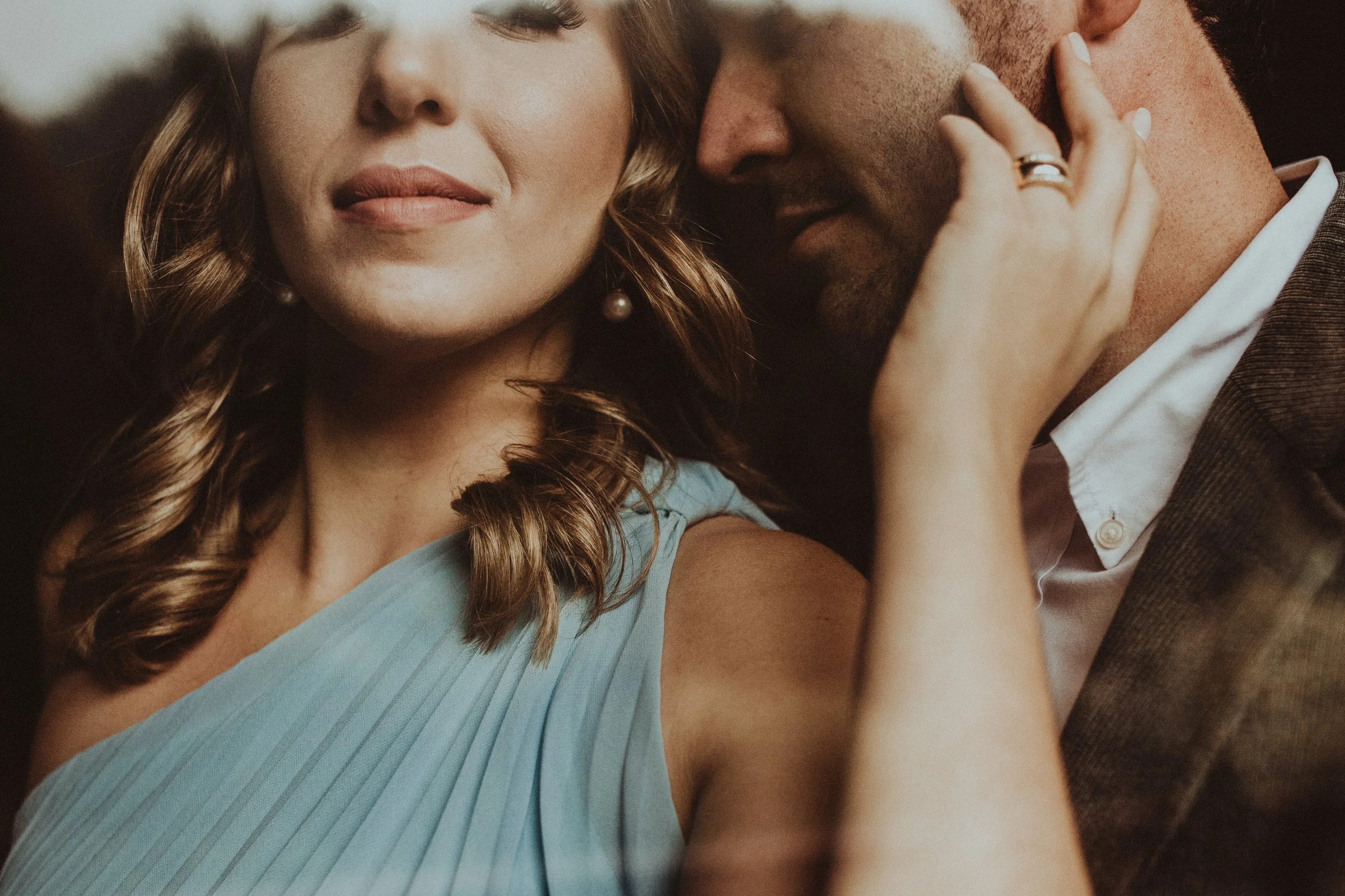 Close-up of a woman with closed eyes and a man with a beard kissing her cheek, with the woman's hand on his face.