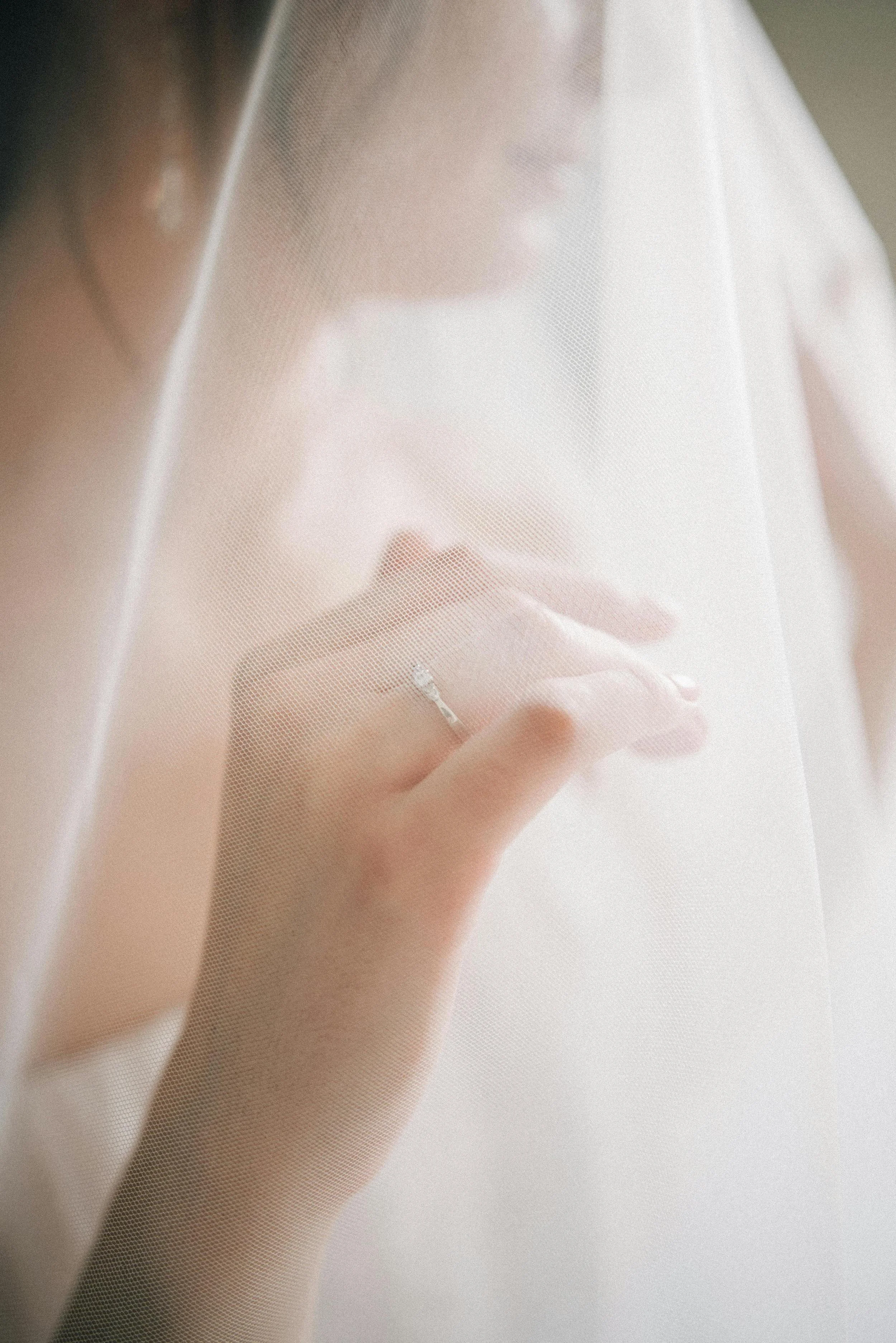 A woman behind a translucent curtain looks at her reflection, her hand touching the curtain, wearing a ring on her finger.