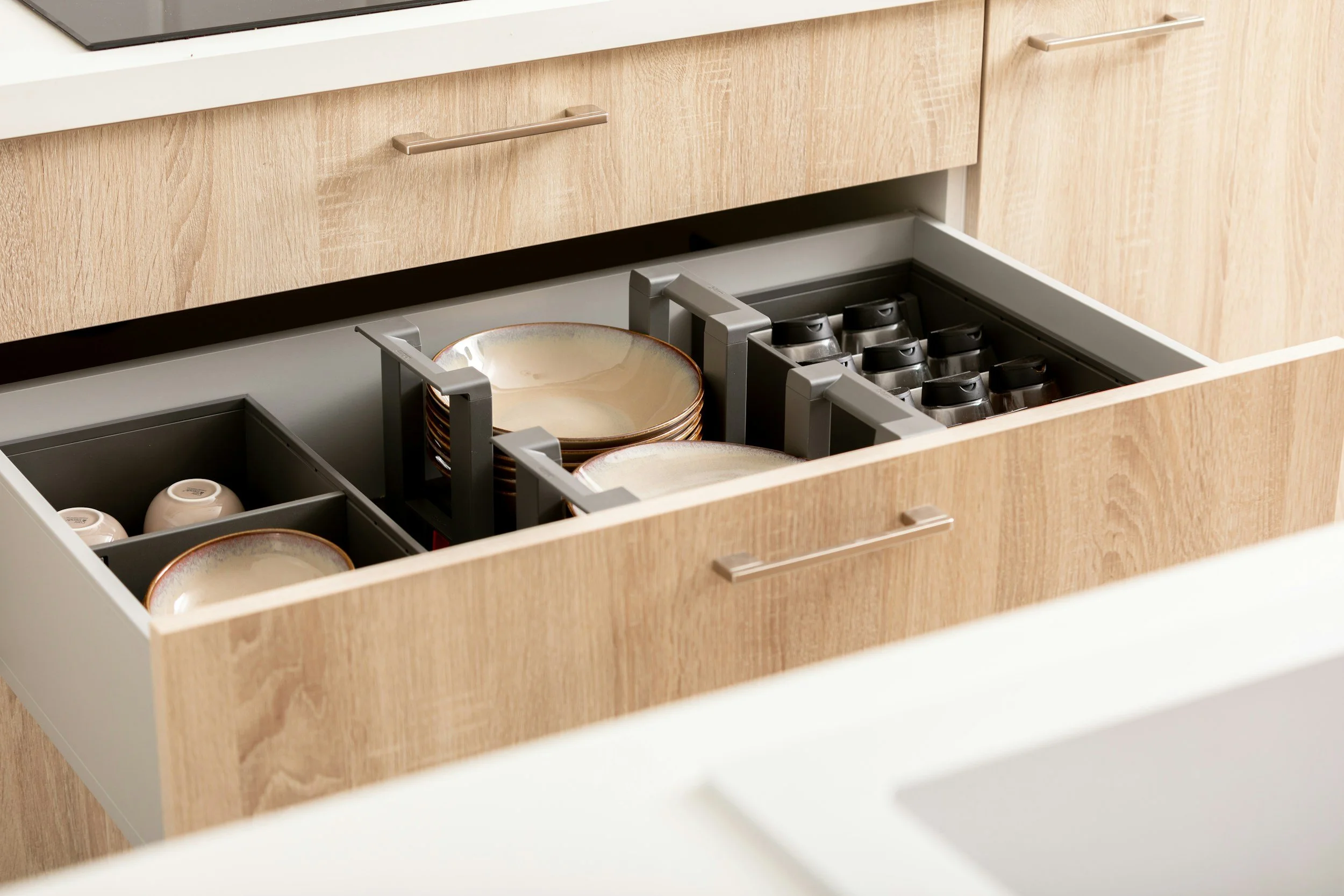 Kitchen drawer containing stacked dishes, bowls, and cups with a cabinet above.