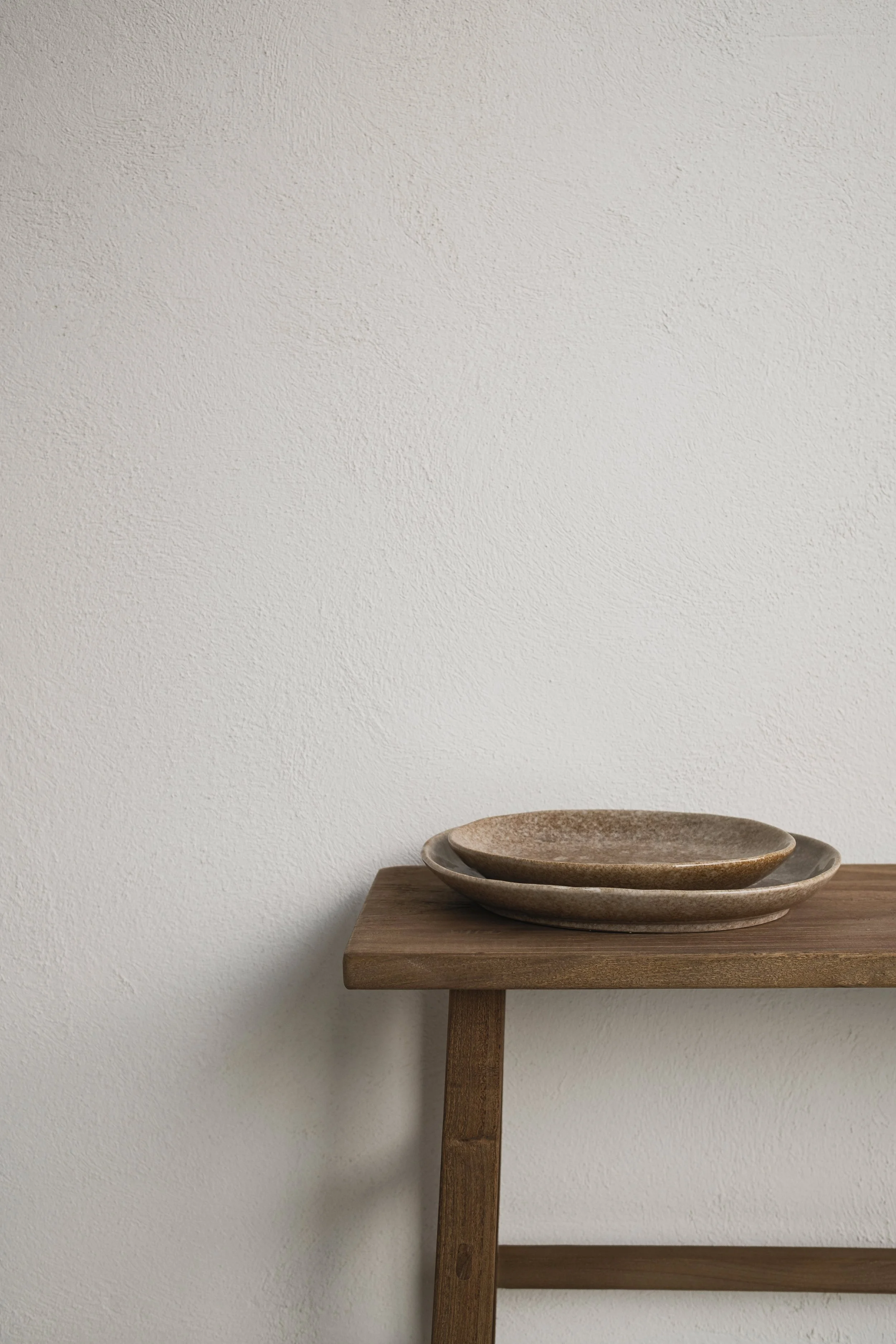 A wooden table with a small shelf on a wall. A set of nested ceramic bowls are placed on the shelf.