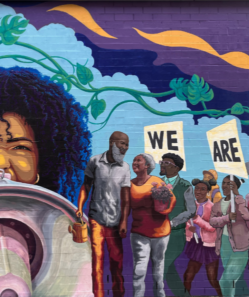A vibrant mural showing a diverse group of people walking together, holding signs that spell out 'WE ARE', with colorful sky and cloud artwork in the background.