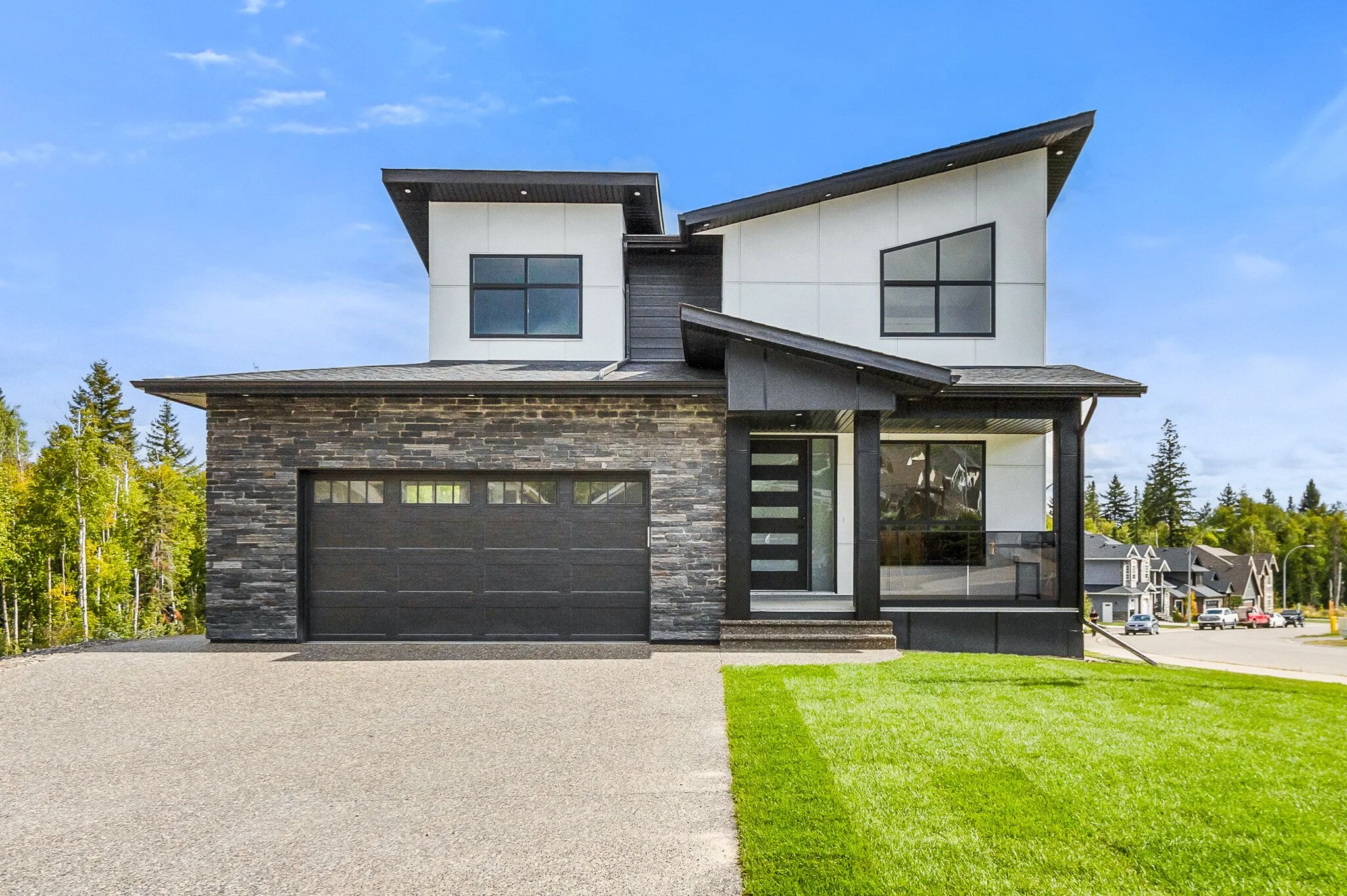 Modern two-story house with a stone and white exterior, large windows, a black garage door, and a front porch, set against a clear blue sky.