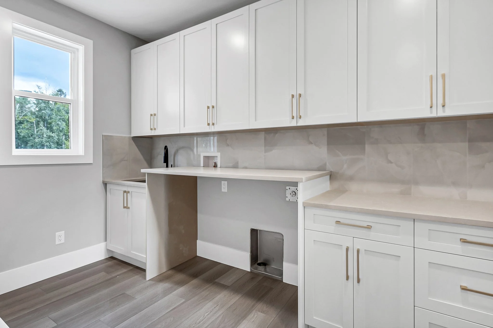 Empty kitchen with white cabinets, a small sink, and a window, with some outlets and a cut-out space for a dishwasher or appliance.