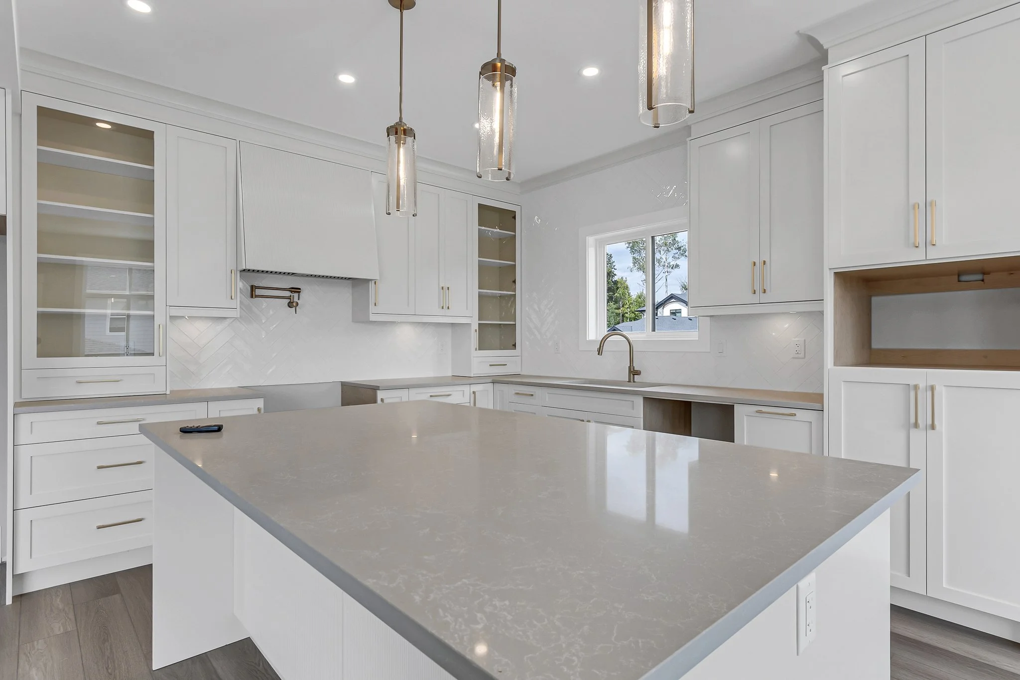 Modern white kitchen with a large island, pendant lighting, and built-in cabinets with glass doors
