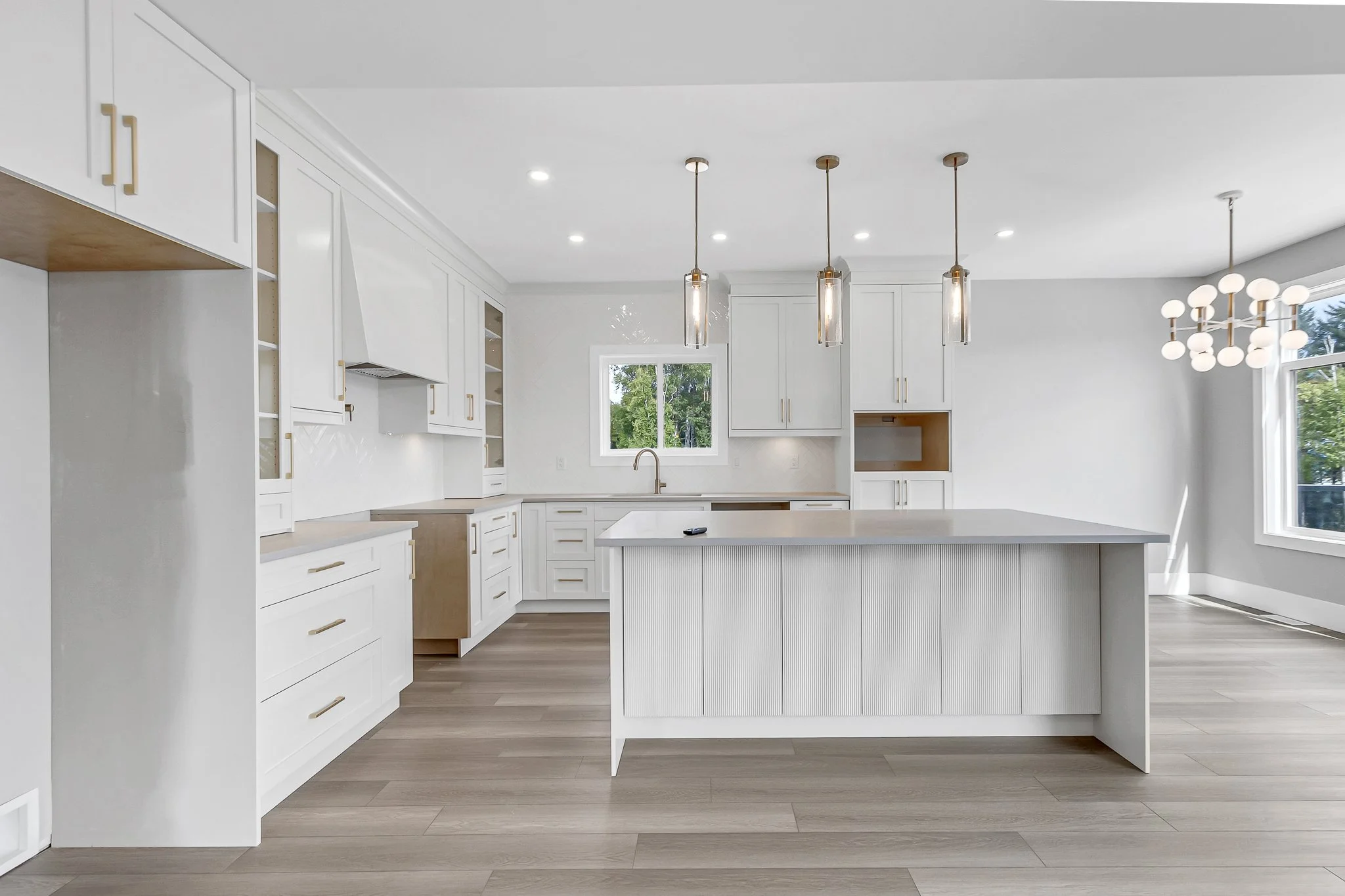 Modern white kitchen with island, pendant lights, and large window.