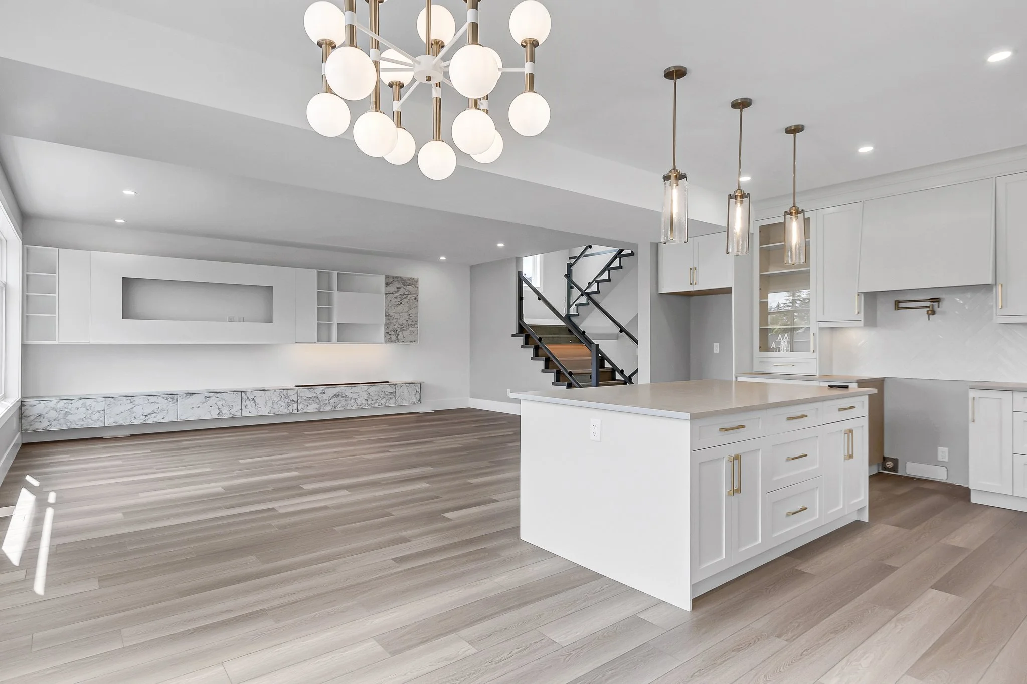 Modern open-concept kitchen and living room with white cabinets, light wood flooring, and contemporary lighting fixtures.