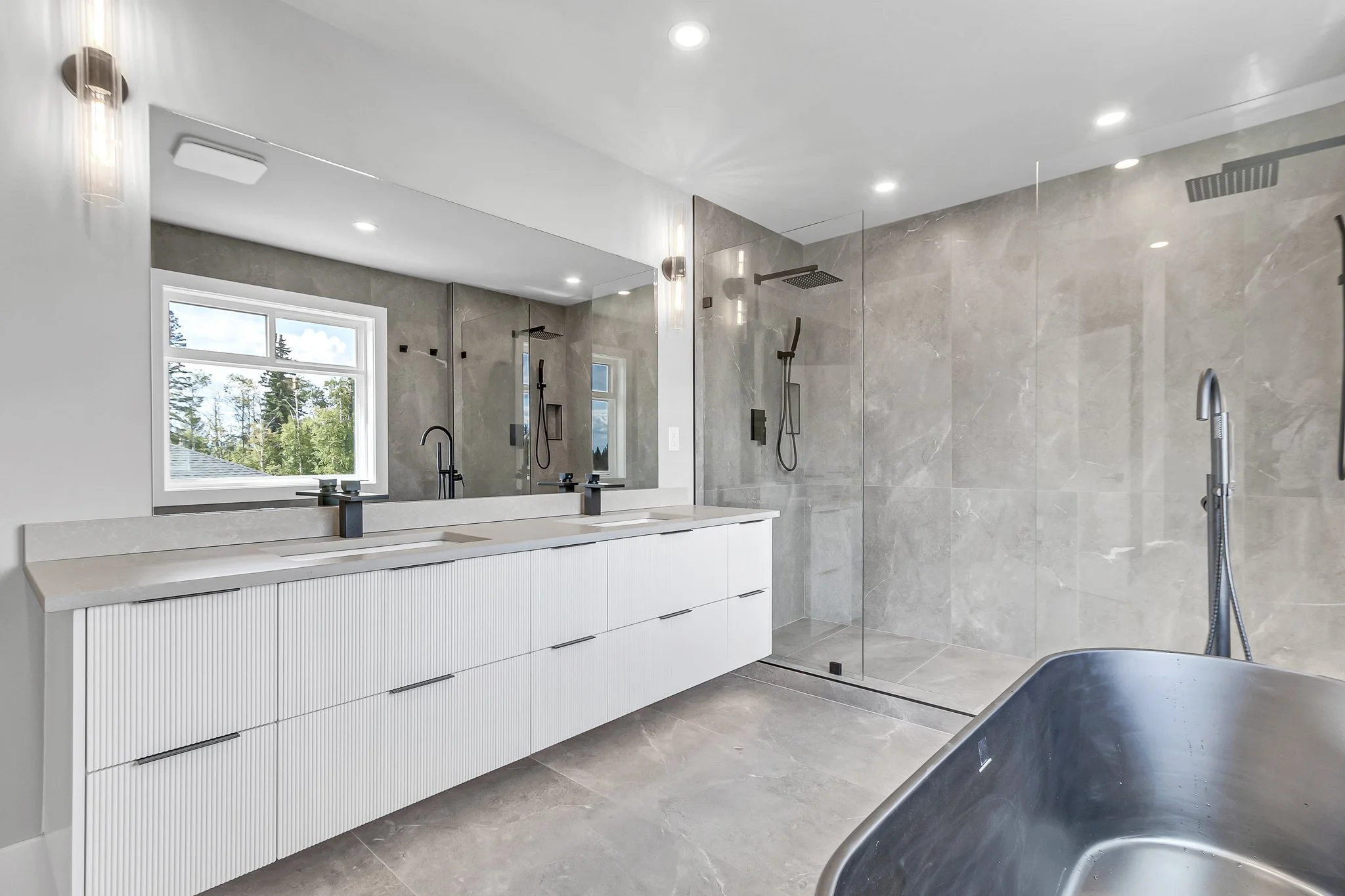 Modern bathroom with large mirror, double sink vanity, walk-in shower with glass enclosure, and a freestanding bathtub.