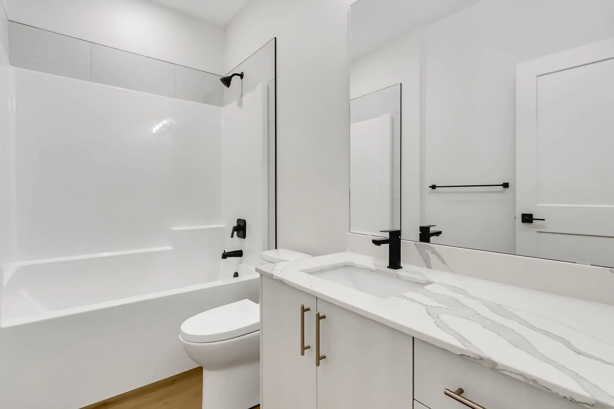 Modern bathroom with white walls, black fixtures, a bathtub, mirror, and a marble countertop.