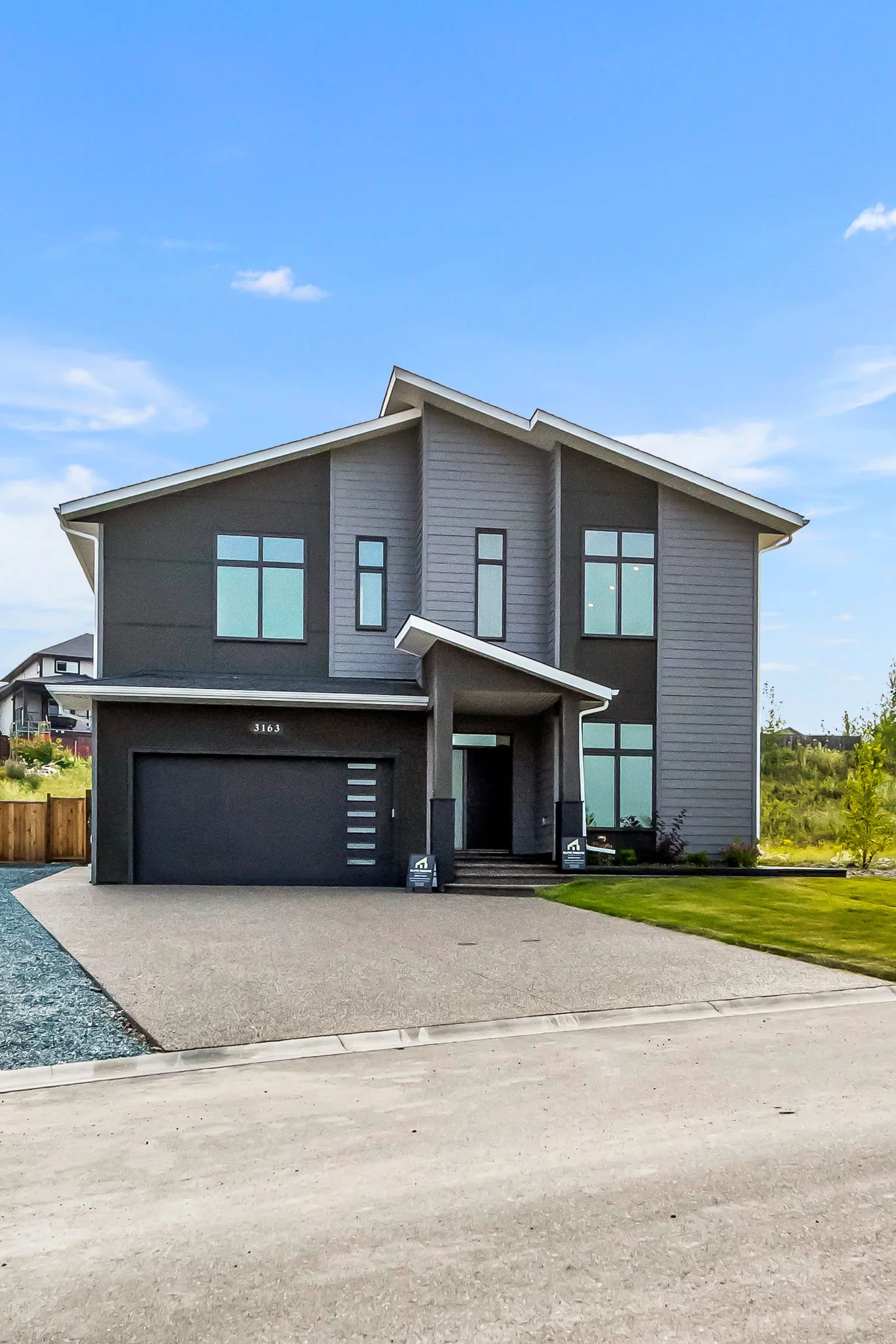 Modern gray two-story house with an attached garage and front steps, green lawn, in a suburban neighborhood with a bright blue sky