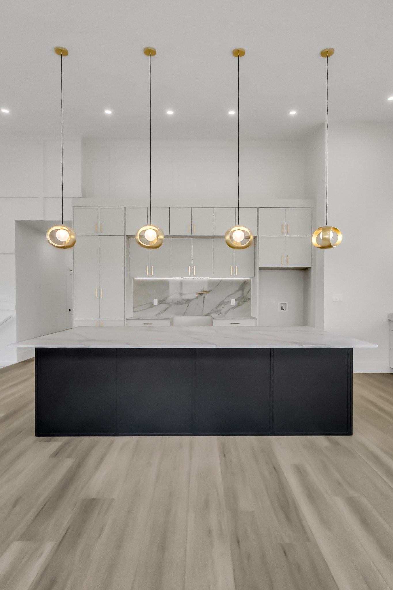 Modern kitchen with cream colored cabinets, a quartz backsplash, a large quartz island and gold pendant lights hanging from the ceiling.