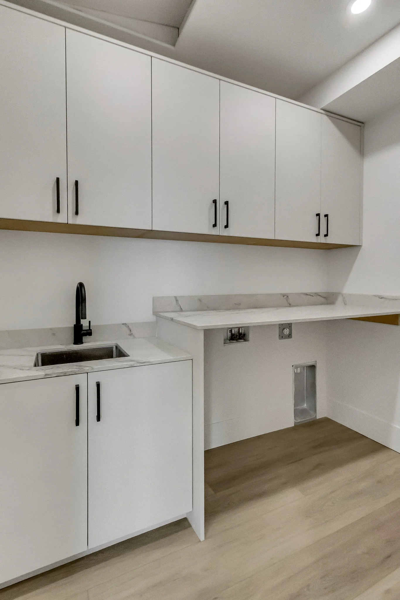 Empty kitchen with white cabinets, a marble countertop, a black faucet, a small sink, and wood flooring.