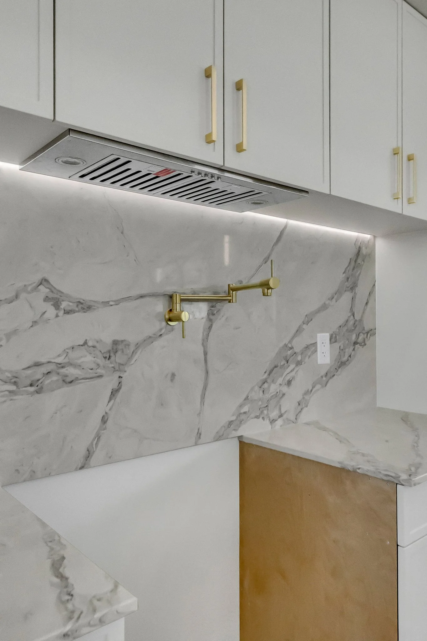 Modern kitchen with white cabinets, gold handles, marble backsplash, and a gold faucet.