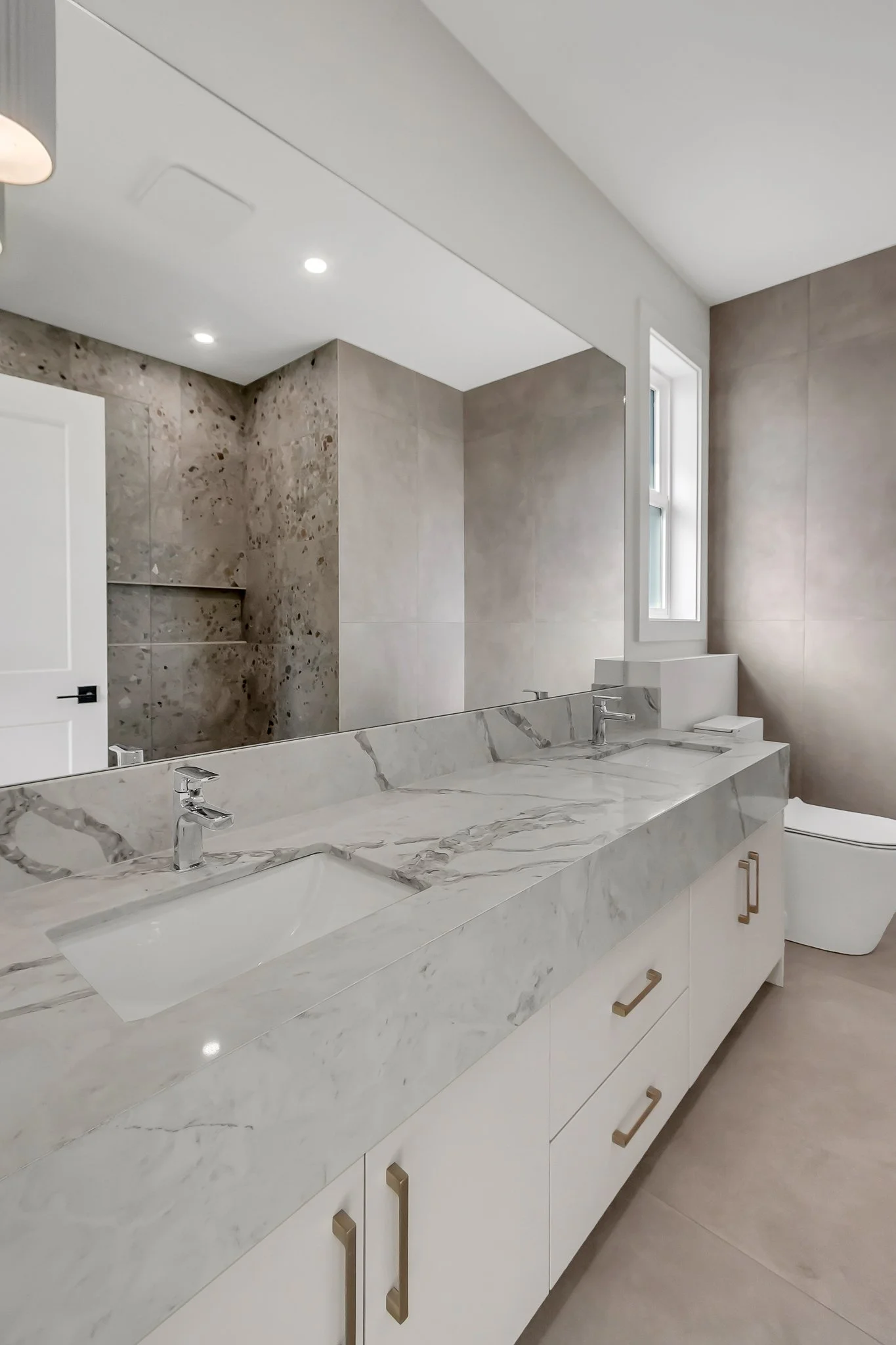 Modern bathroom with quartz double sink vanity, large mirror, tiled walls, window, and a white toilet.