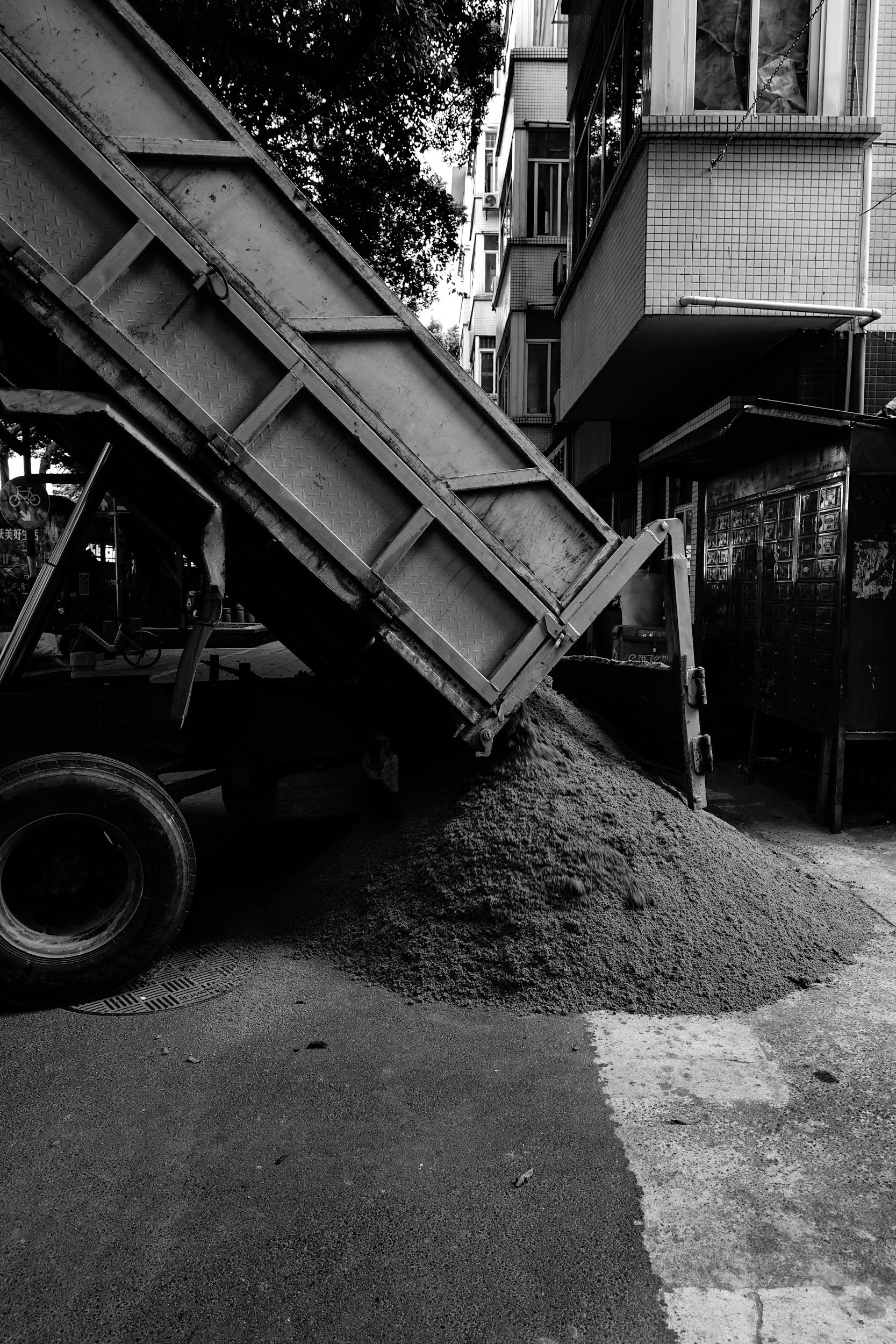 A construction site on a city street where a truck is dumping gravel or sand onto the ground.