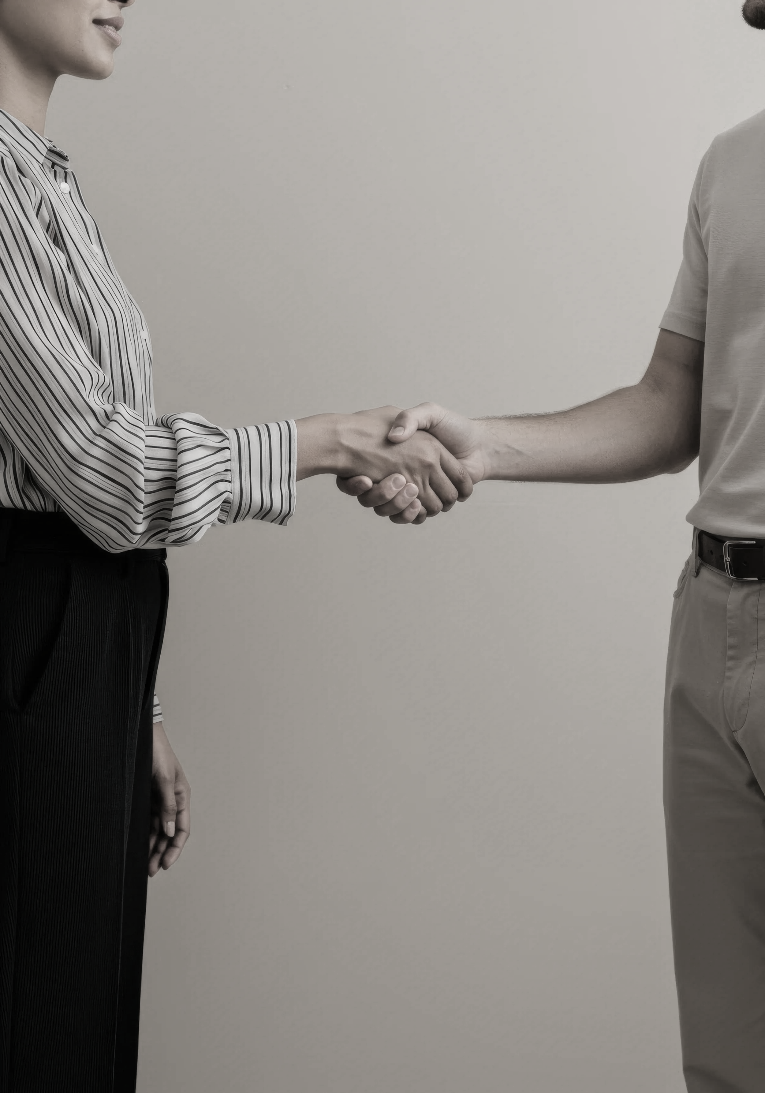 Two people shaking hands, one wearing a striped shirt and black pants, the other in a plain t-shirt and light-colored pants, against a plain background.
