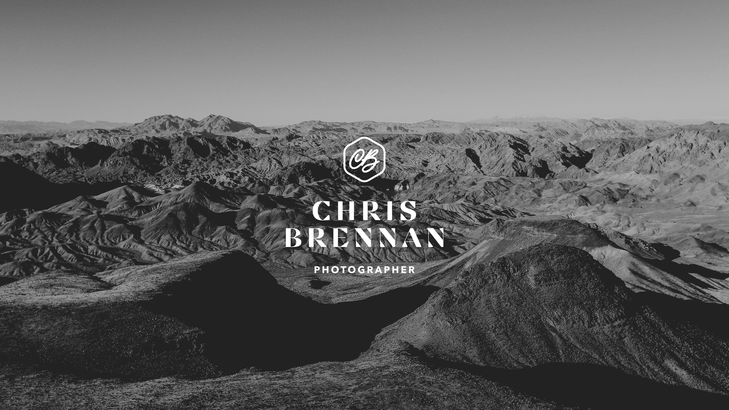Black and white photo of rugged mountain landscape with sharp ridges and valleys, overlaid with text 'Chris Brennan Photographer' and a logo.