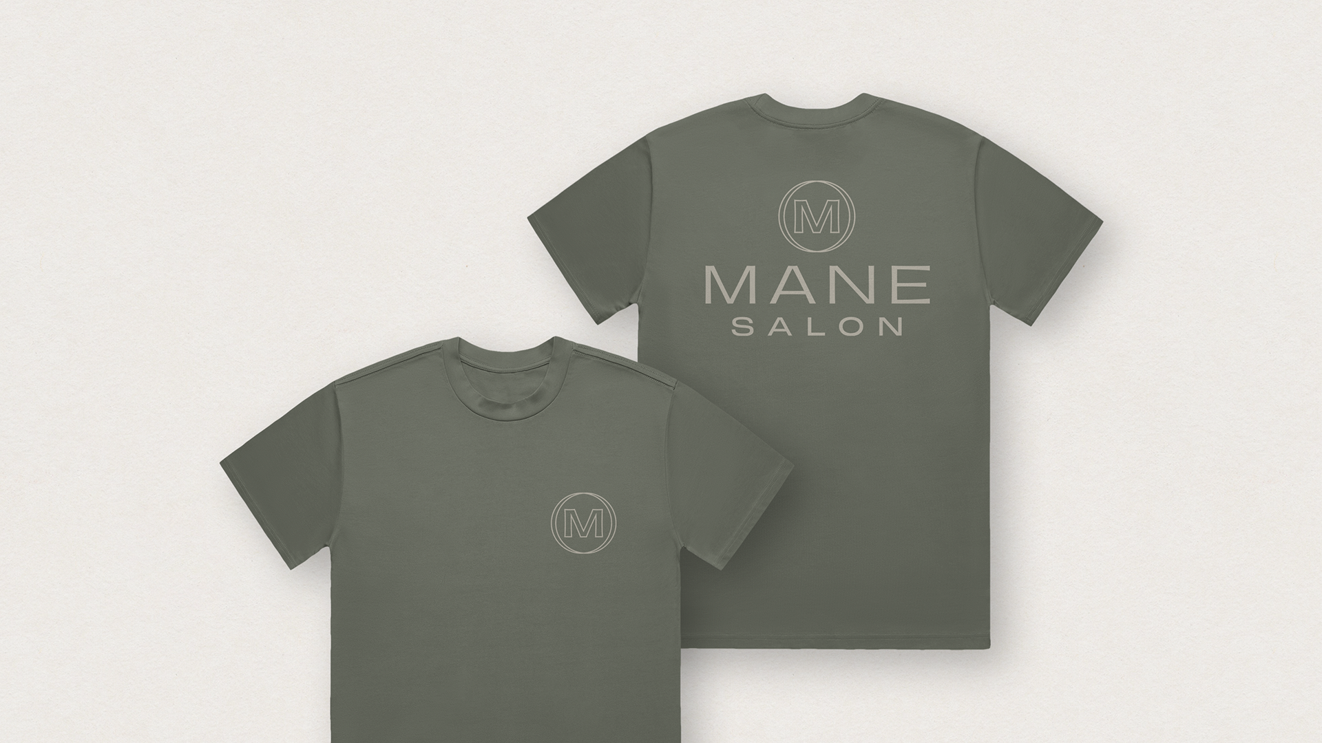 Gray T-shirts with a circular logo and the words 'MANE SALON' on the back of one shirt and a smaller logo on the front of another shirt, laid flat on a light background.