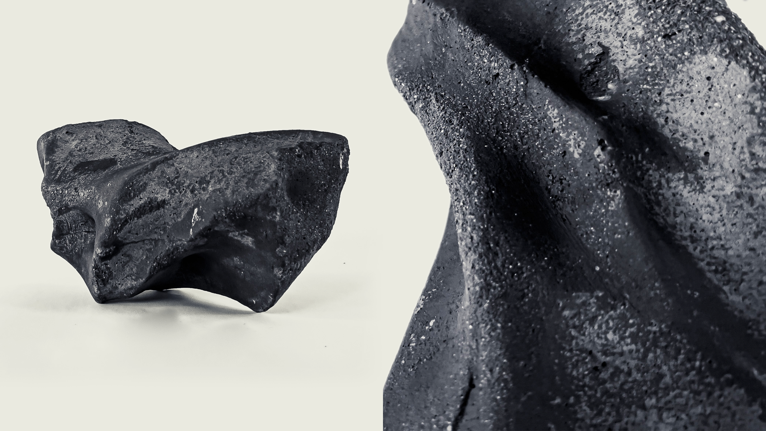 Close-up shot of a small black volcanic rock and a larger rough black stone against a plain background.