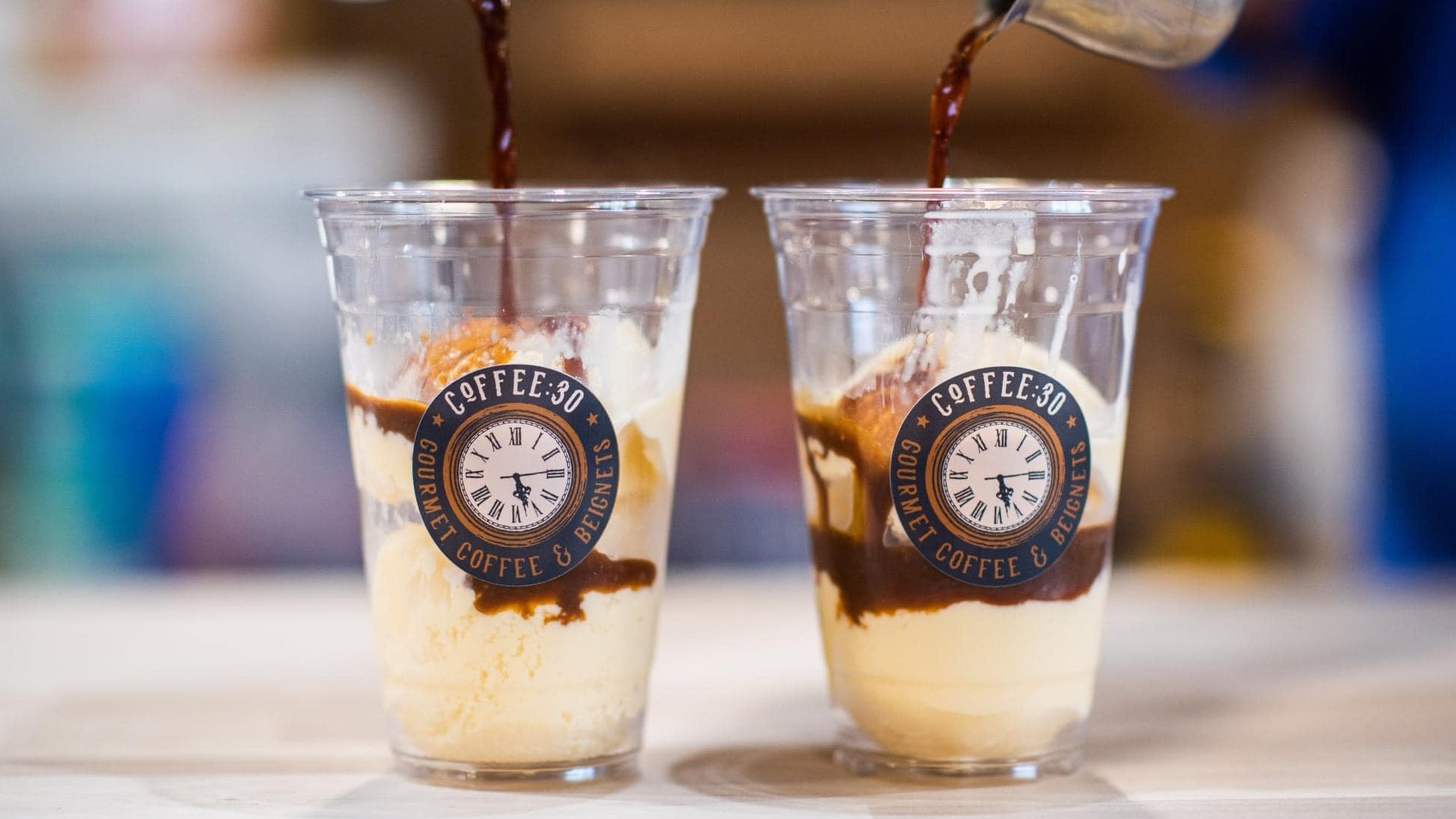 Two clear plastic cups filled with vanilla ice cream, chocolate syrup, and a sticker with a clock face and the text "COFFEE:30".