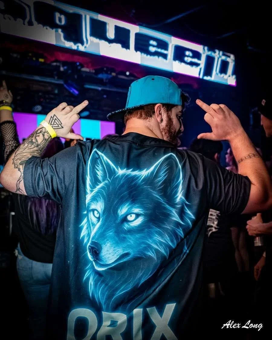 Person wearing a black shirt with a glowing blue wolf face on the back, standing in a nightclub or concert with neon signs and purple lighting.