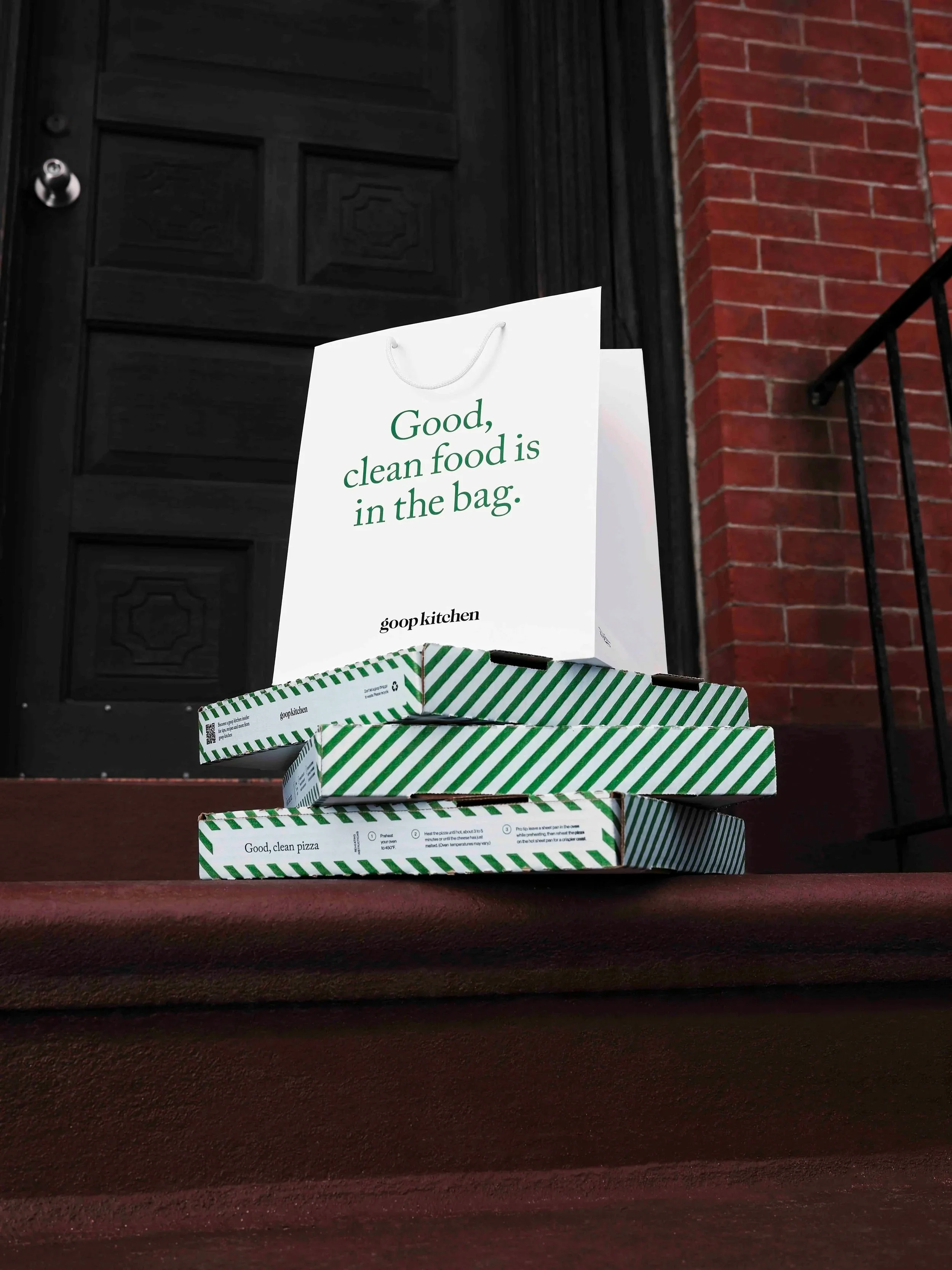 Pizza boxes stacked on front porch stairs with a sign that reads 'Good, clean food is in the bag.' and a black front door with a brick wall to the side.