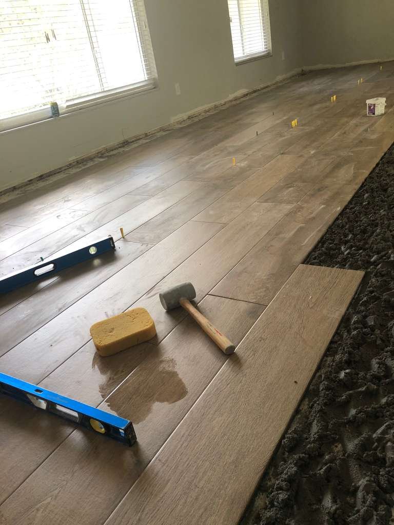 Installing wooden floorboards in a room with renovation tools including a rubber mallet, level, sponge, and spacers.