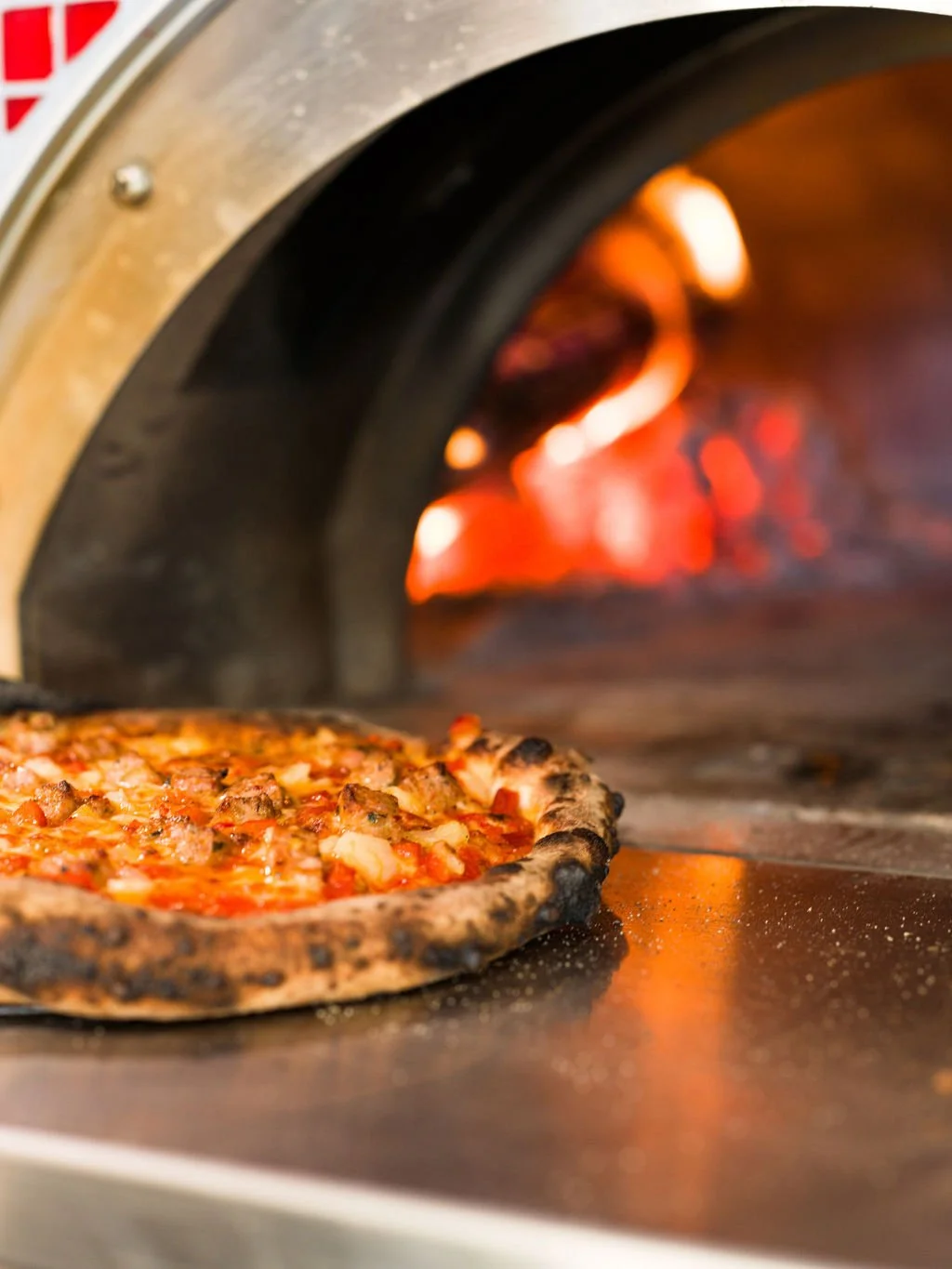 Pizza baking in a hot pizza oven with a blazing fire inside.