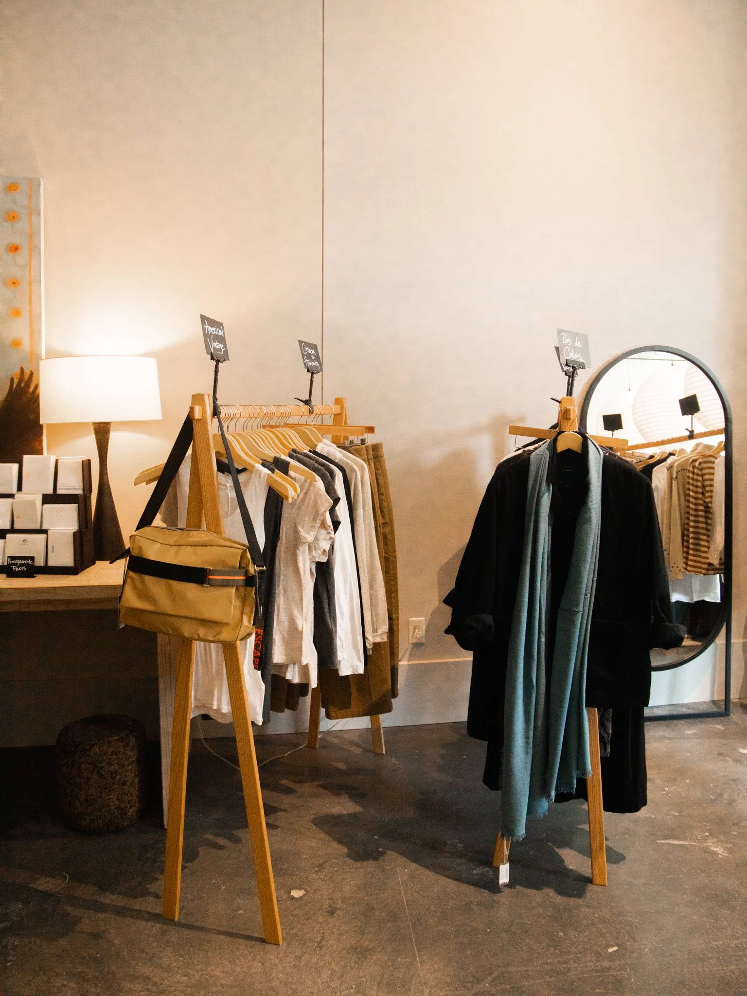 Clothing display in a store with racks of shirts and jackets, a mirror, and a yellow bag on a wooden stand.