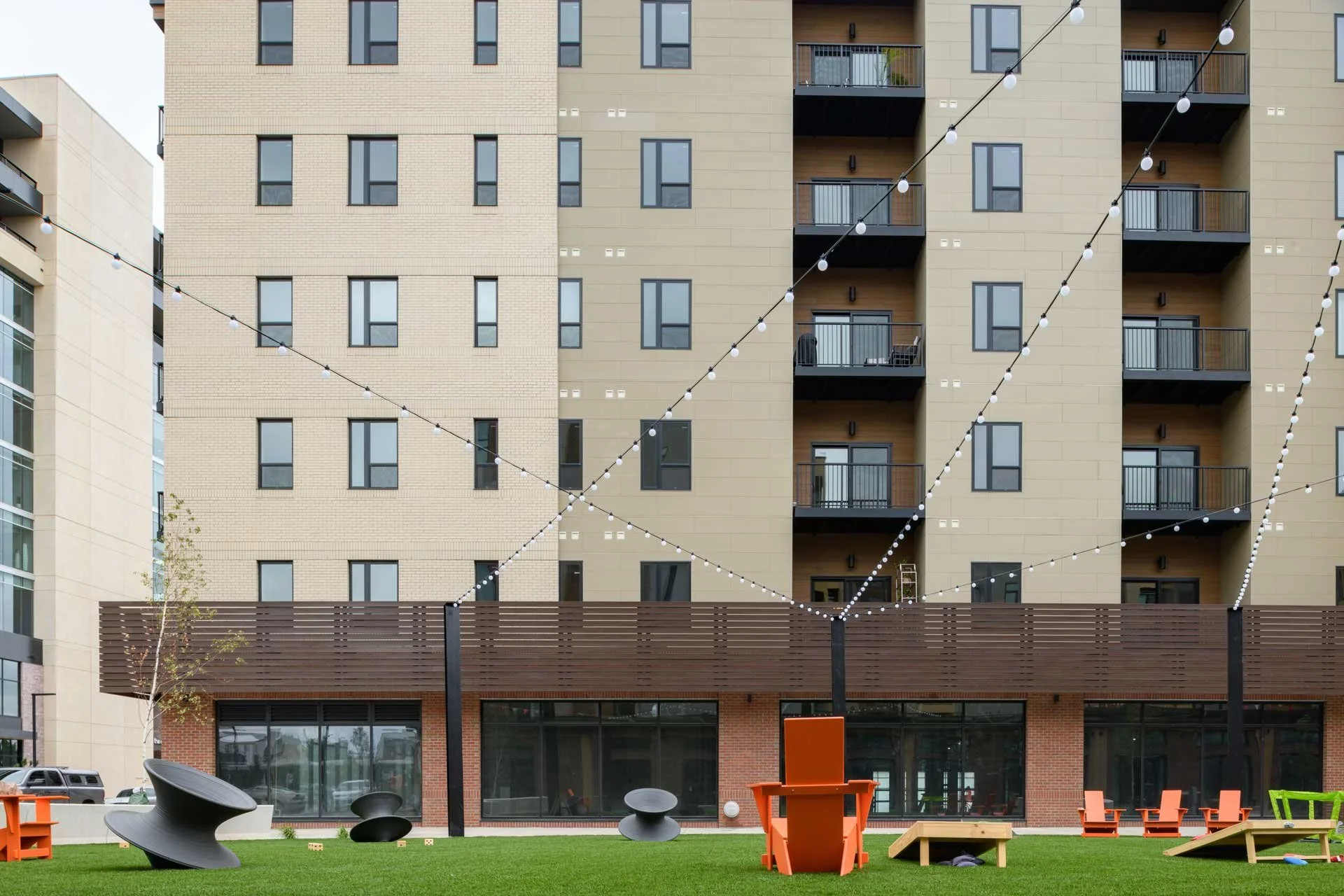 Image of Cherapa Place. A modern residential building with multiple balconies, string lights overhead, and outdoor furniture on a green lawn with playground equipment.