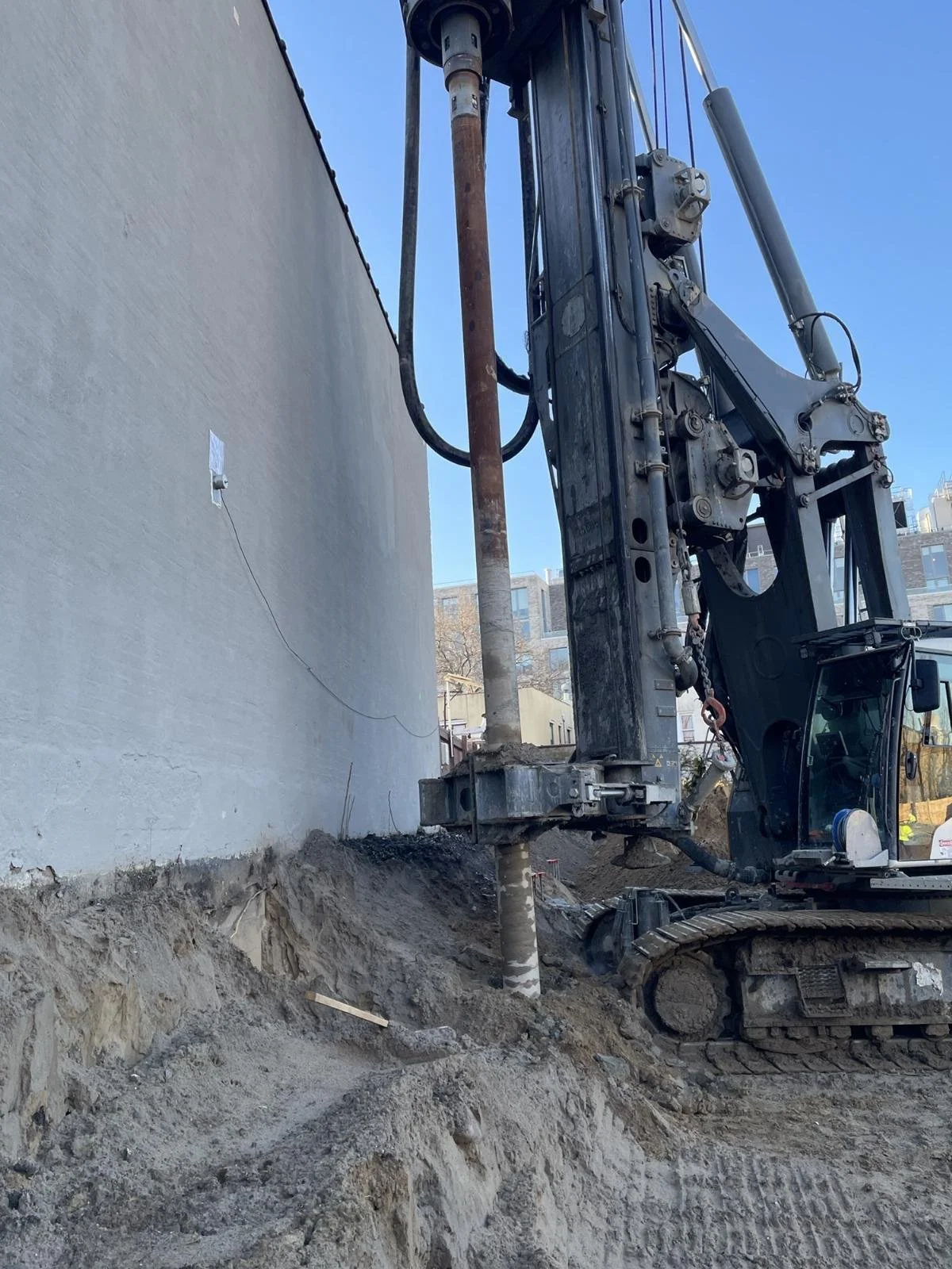 A construction site with a large drilling machine next to a building wall, excavating the ground.