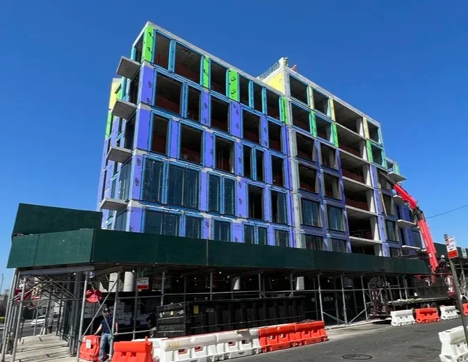 Under construction multi-story building with colorful framing, scaffolding, construction workers, and equipment