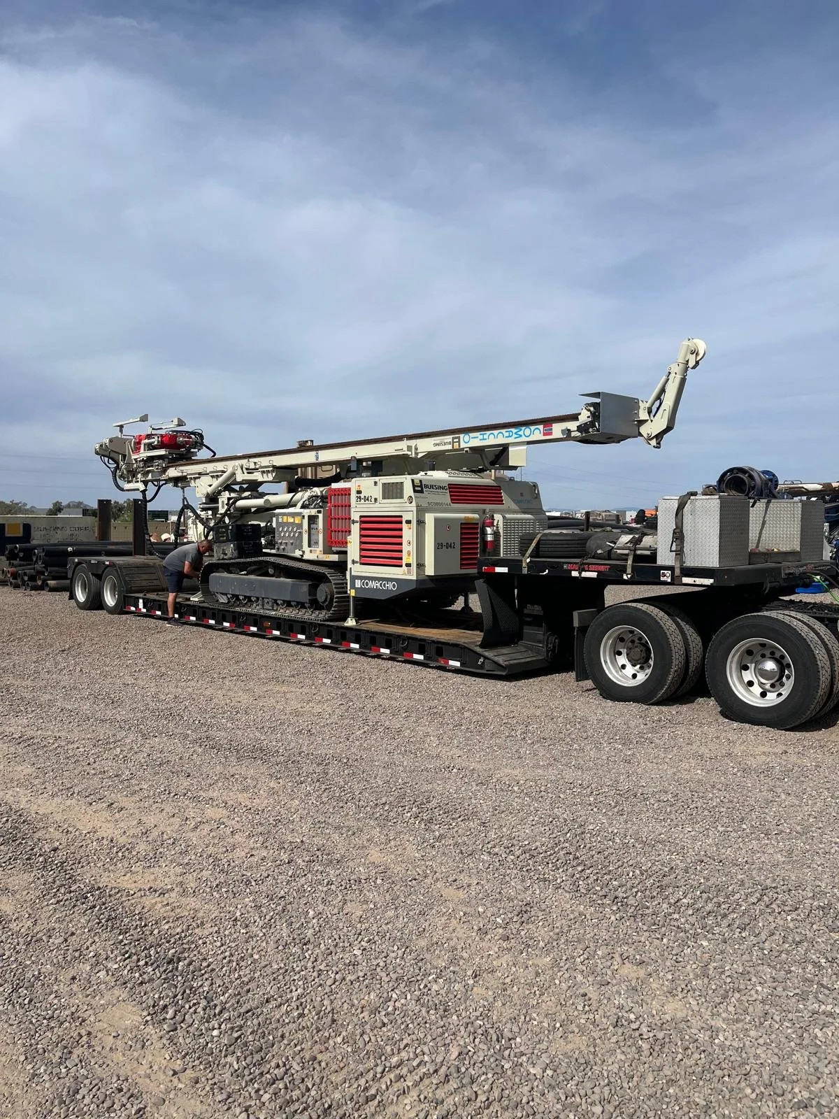 A large industrial crane mounted on a trailer, with a person working nearby in an outdoor gravel lot