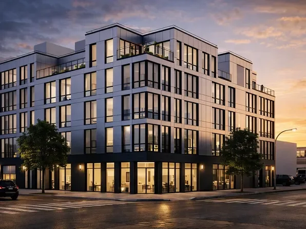 Modern multi-story apartment building with large windows and balconies, set against a sunset sky.