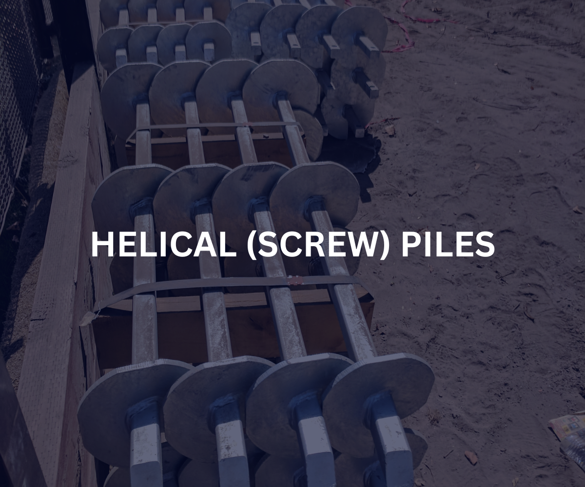 Stacked helical screw piles with metal blades on a construction site with dirt ground.