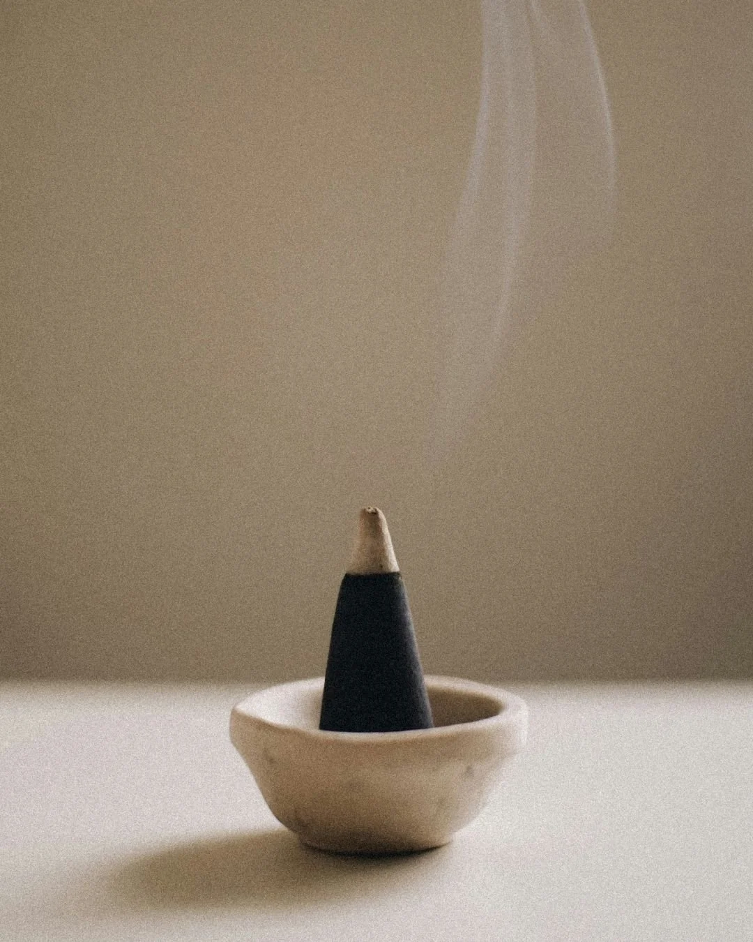 Incense cone sitting in a small ceramic dish, with smoke rising from the tip.