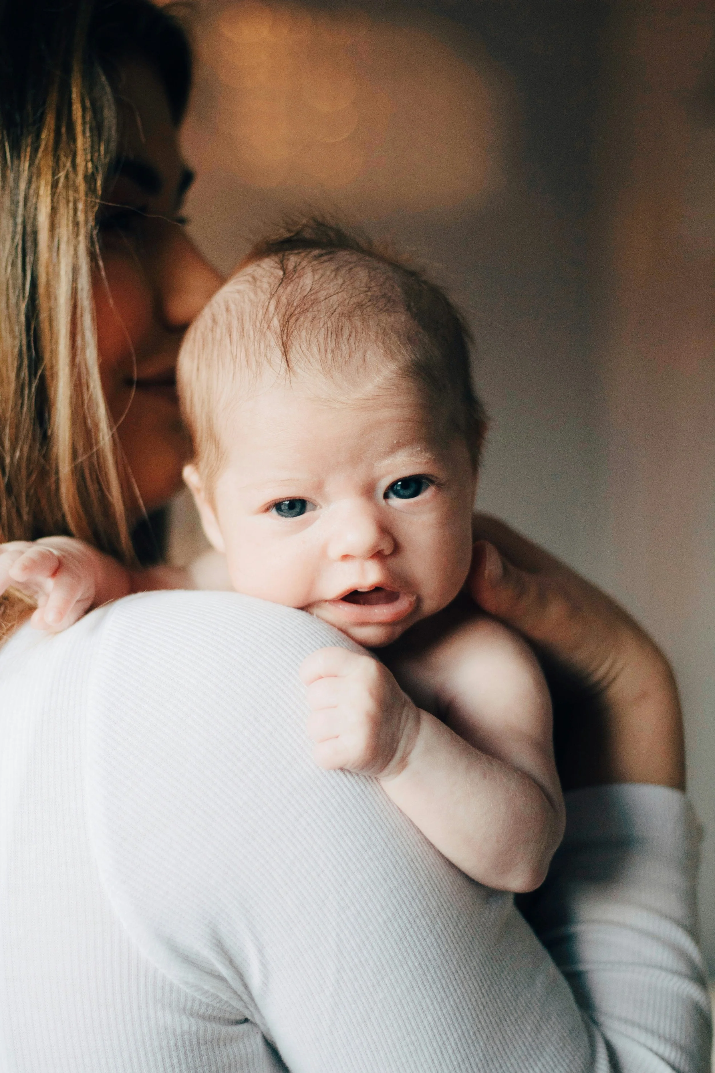A woman holding a young child with blue eyes and light skin, close to her face, in warm indoor lighting. Soul Held | Reiki • Energy Healing • Intuitive Guidance