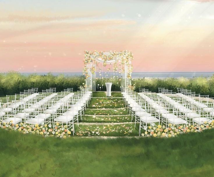 A beautifully decorated outdoor wedding ceremony setup on grass with white chairs arranged in rows on either side of a green aisle. An arch decorated with white confetti and flowers stands at the front near a white podium, with a floral border along the aisle. The background features a sunset over the ocean with a soft pink and orange sky.