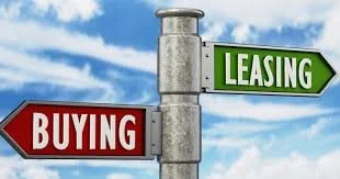 Signpost with arrows for 'Buying' in red pointing left and 'Leasing' in green pointing right, against blue sky with clouds.