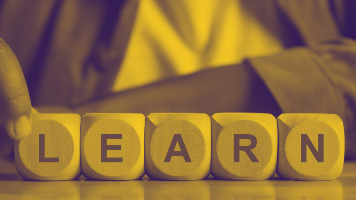 Wooden blocks spelling out the word "LEARN" on a table with a person in the background.