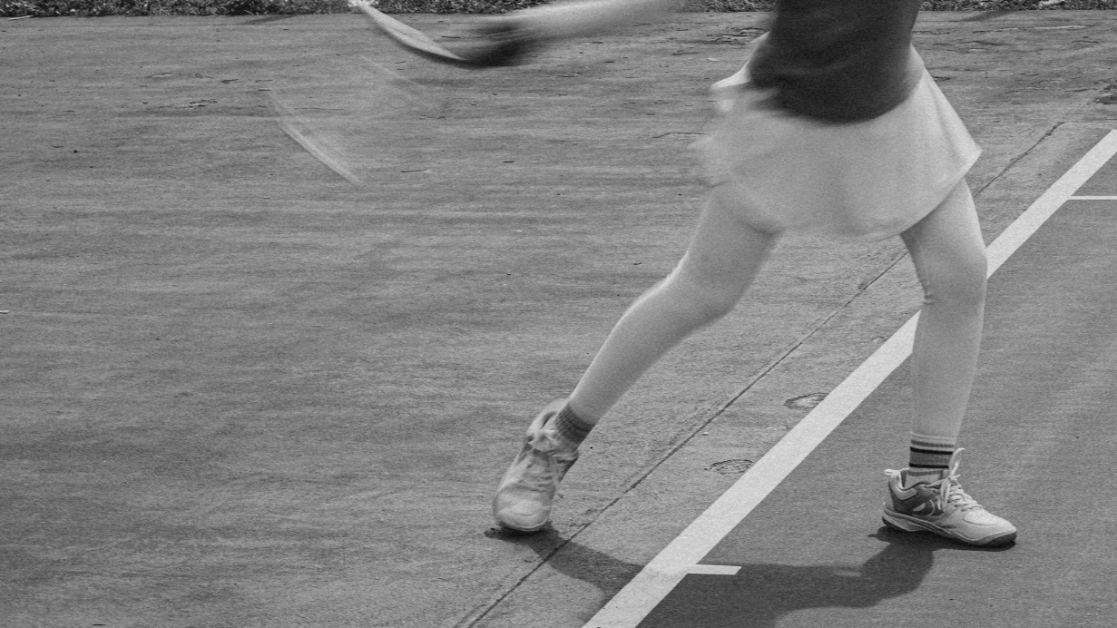 A person playing tennis on a court, wearing athletic shoes, a skirt, and striped socks. The person is preparing to hit the ball with a tennis racquet.
