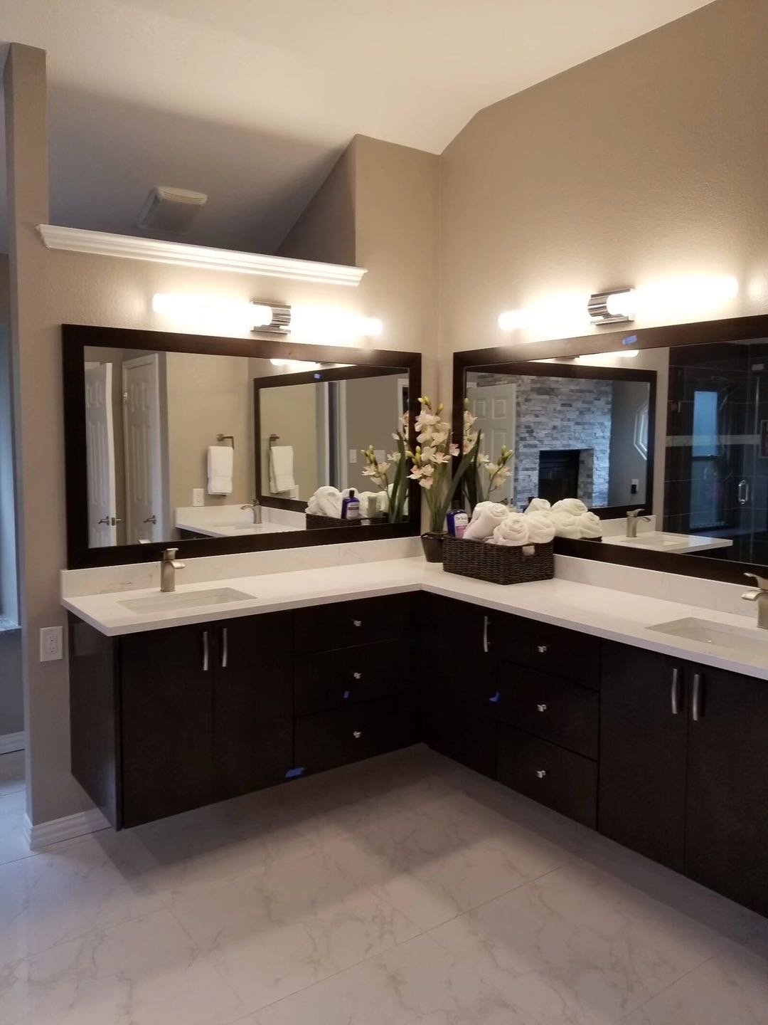Bathroom with dual sinks, large mirrors, dark wood cabinets, tile floor, flowers, and folded towels.