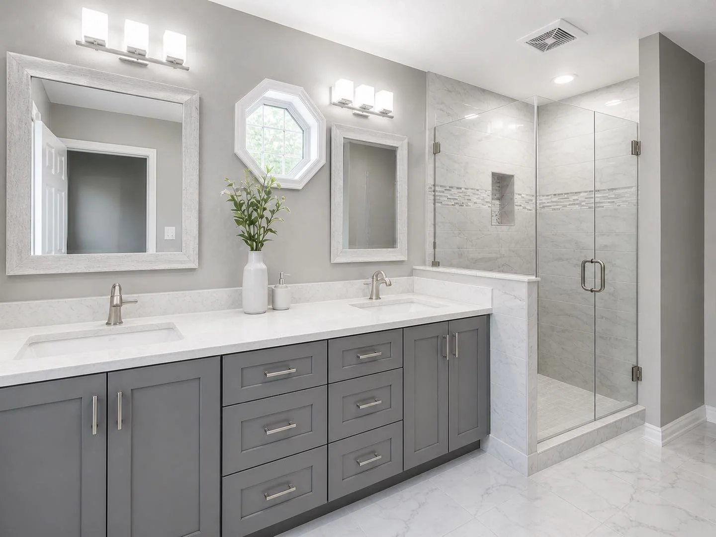 Modern bathroom with gray cabinetry, white marble countertop, two sinks, large mirrors, a small window, decorative plant, and a glass-enclosed shower with marble tiles.