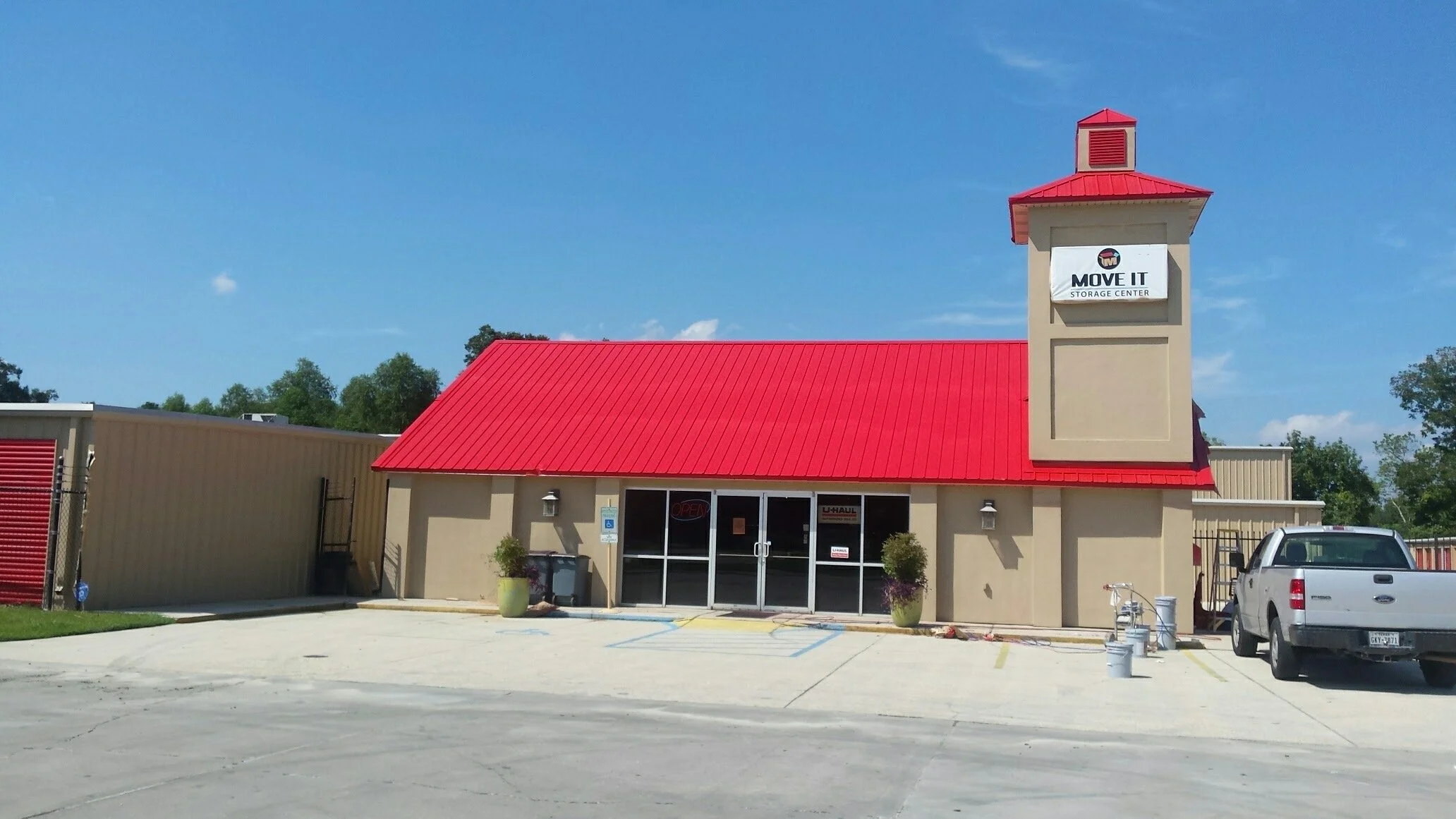 A small beige building with a red metal roof, large front doors, and a sign that reads 'Move It Storage Center.'