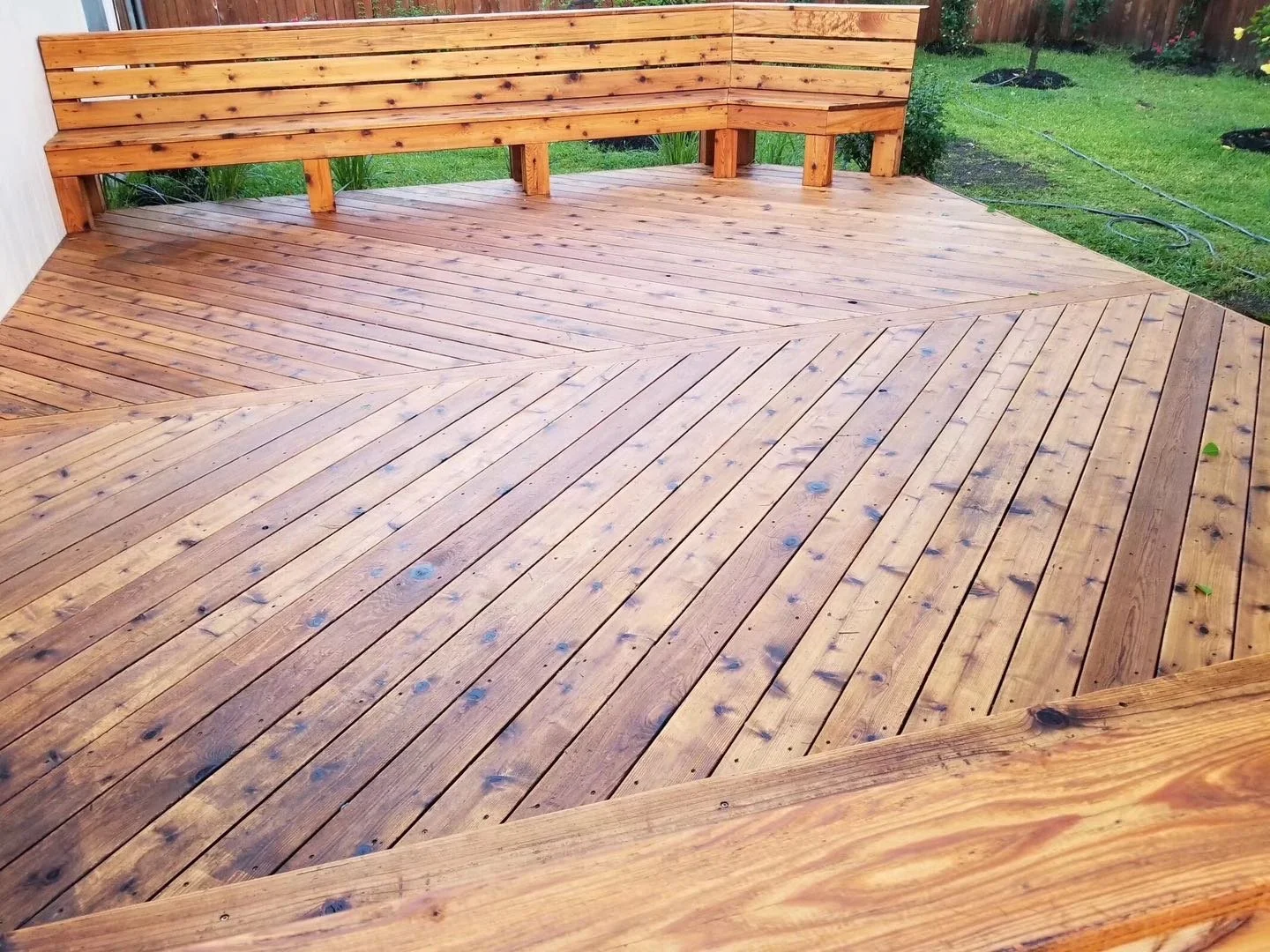 A home wooden deck with a built-in bench, surrounded by a grassy backyard.