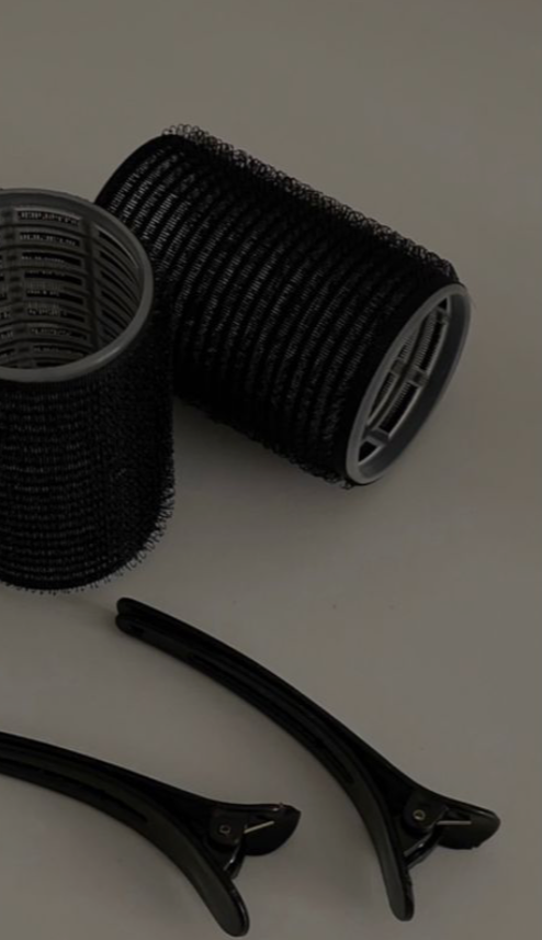 Two cylindrical hair rollers and a pair of black hair clips on a white surface.