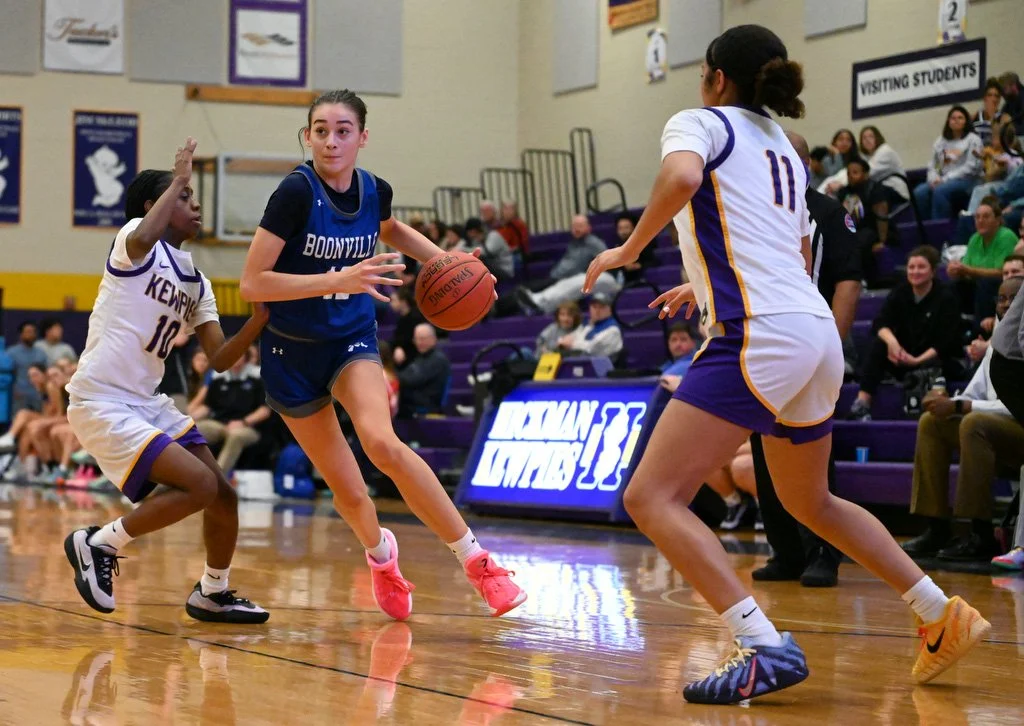 Boonville freshman Harper Lowe drives through Hickman sophomore Bayleigh Bluitte, left, and freshman London Stemmons, right, for a lay-up on Tuesday at Hickman High School in Columbia, Mo. The Kewpies celebrated senior night before securing a 69-55 v
