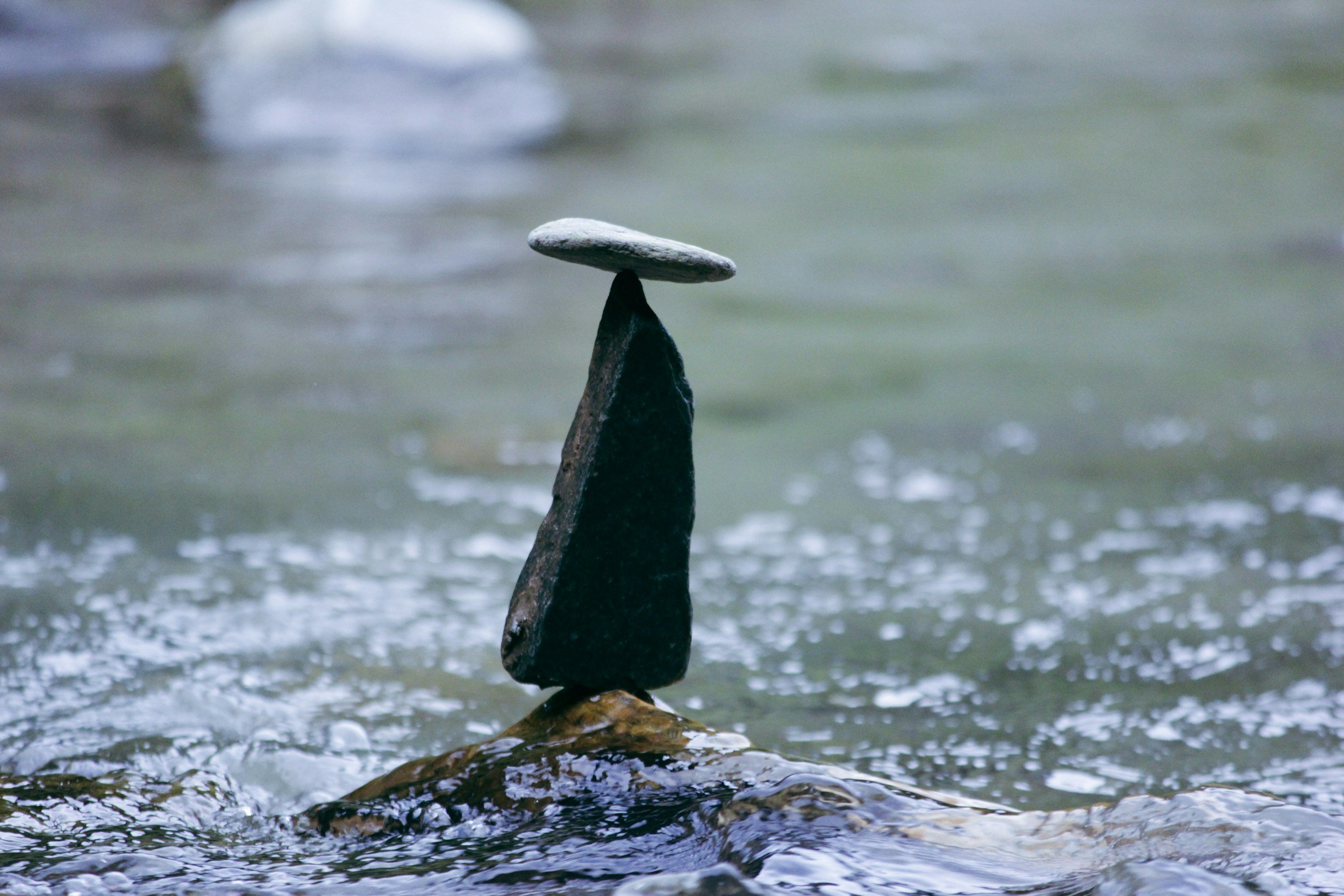 A rock balancing on top of another rock in a river with water flowing around.