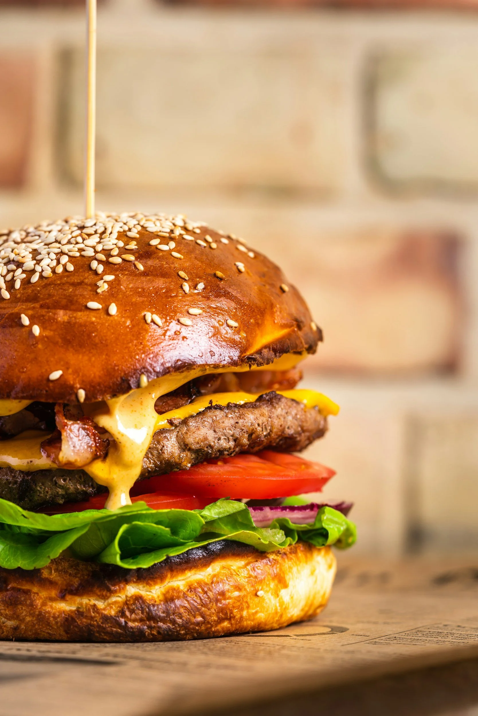 A close-up of a cheeseburger with lettuce, tomato, onion, a beef patty, melted cheese, and a sesame seed bun, held together with a toothpick.