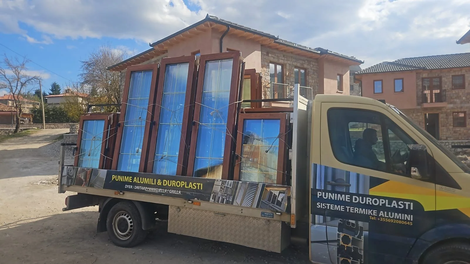 A truck loaded with blue and brown framed aluminum and glass windows parked in front of residential houses.
